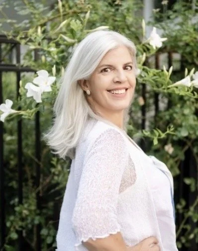 A divorce attorney with silver hair dress in white standing outdoors in front of greenery and white flowers