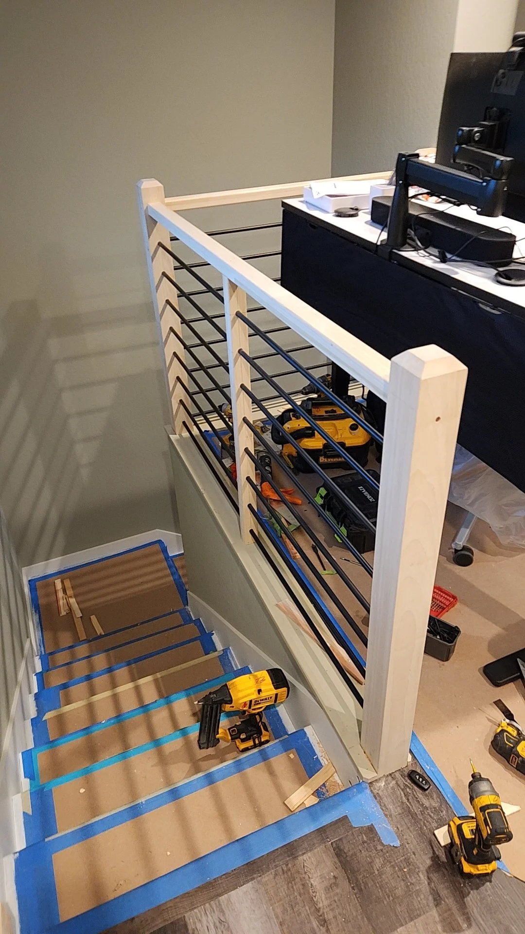 A partially assembled wooden and metal bed frame with tools and supplies on and around it, including a cordless drill, on a hardwood floor in a room with gray walls.