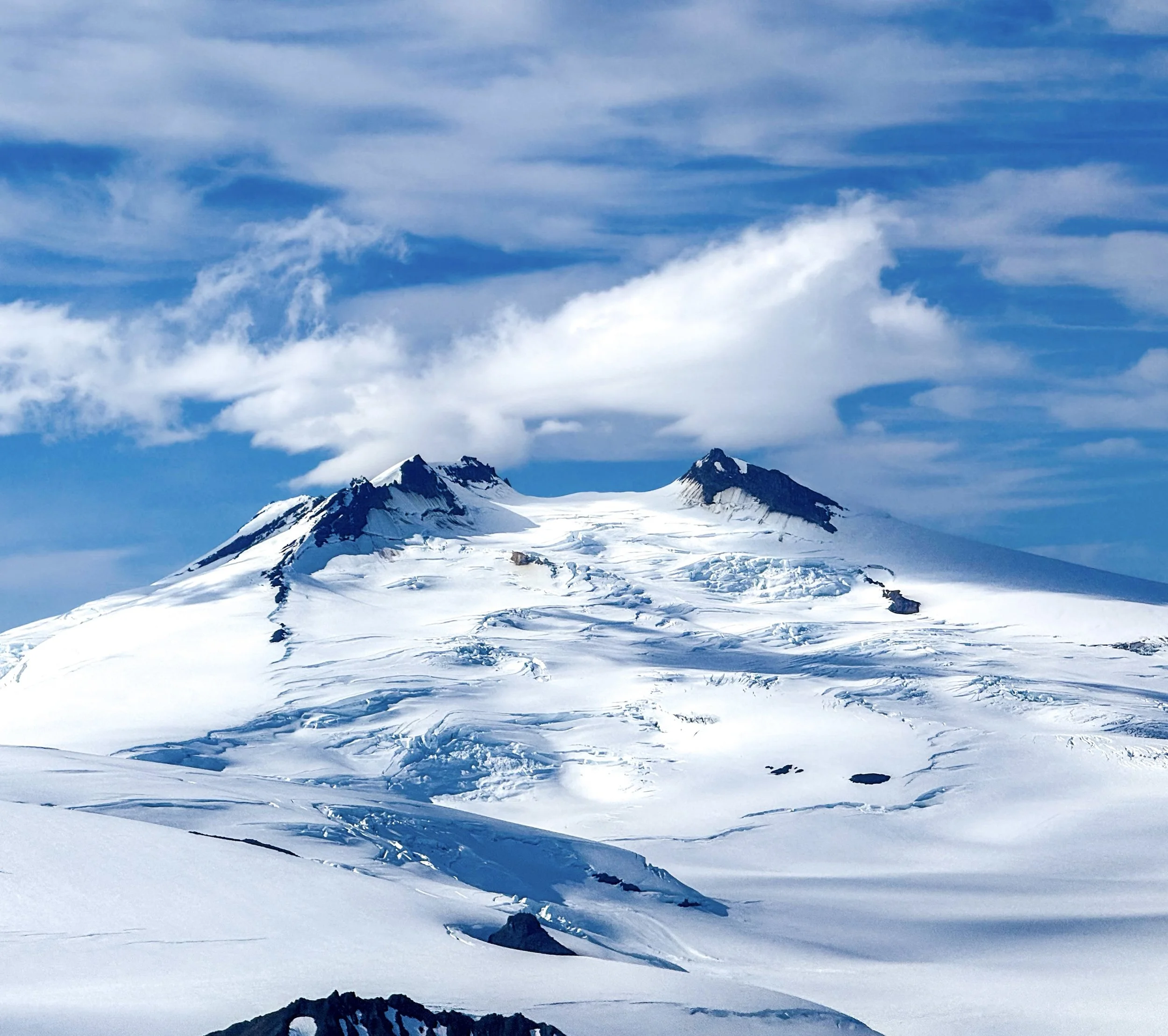 Snow-covered mountain with two peaks under a cloudy sky.