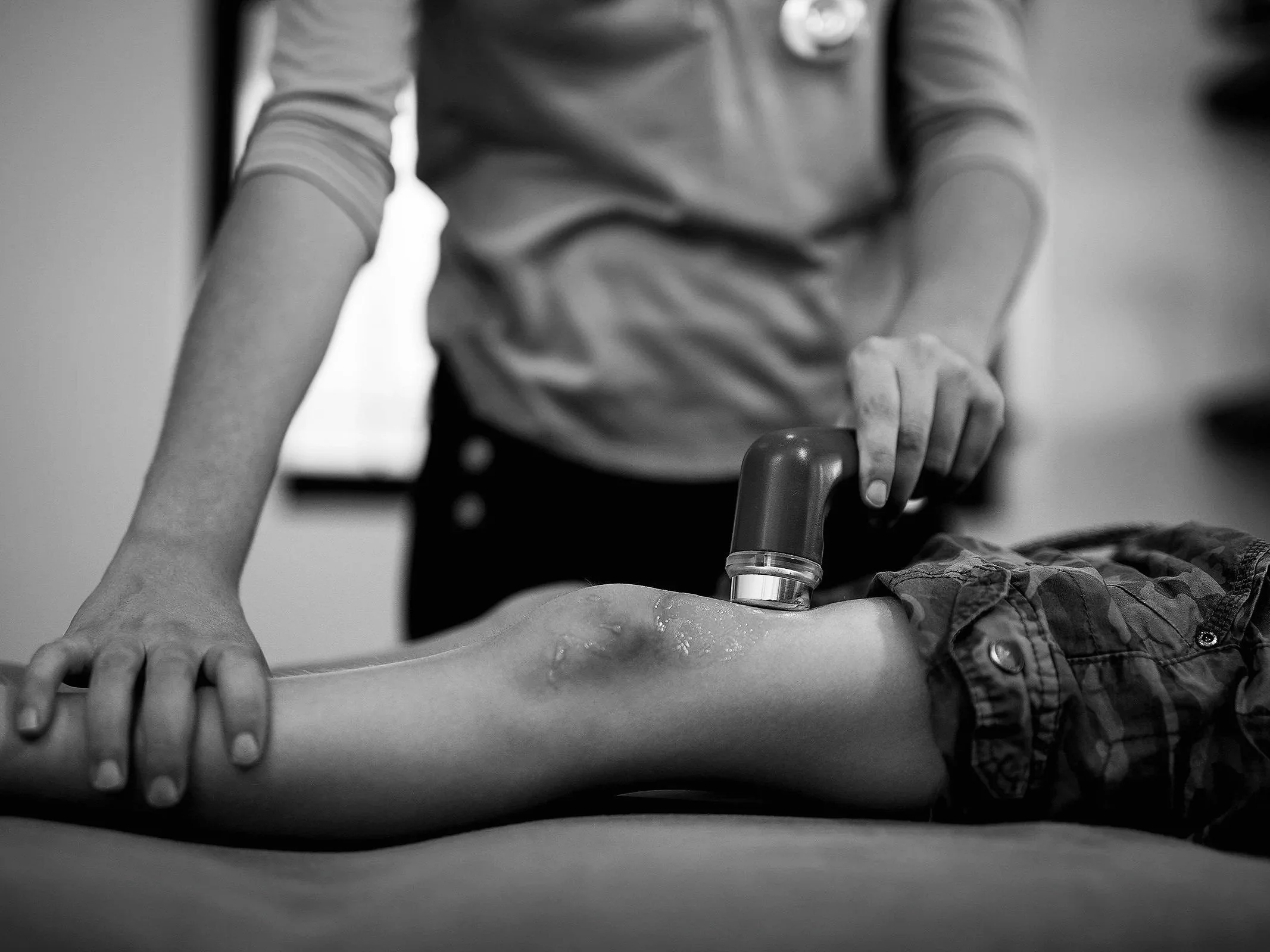 A person performing CPR on a child, using a resuscitation device on the child's leg while the child lies on a flat surface.