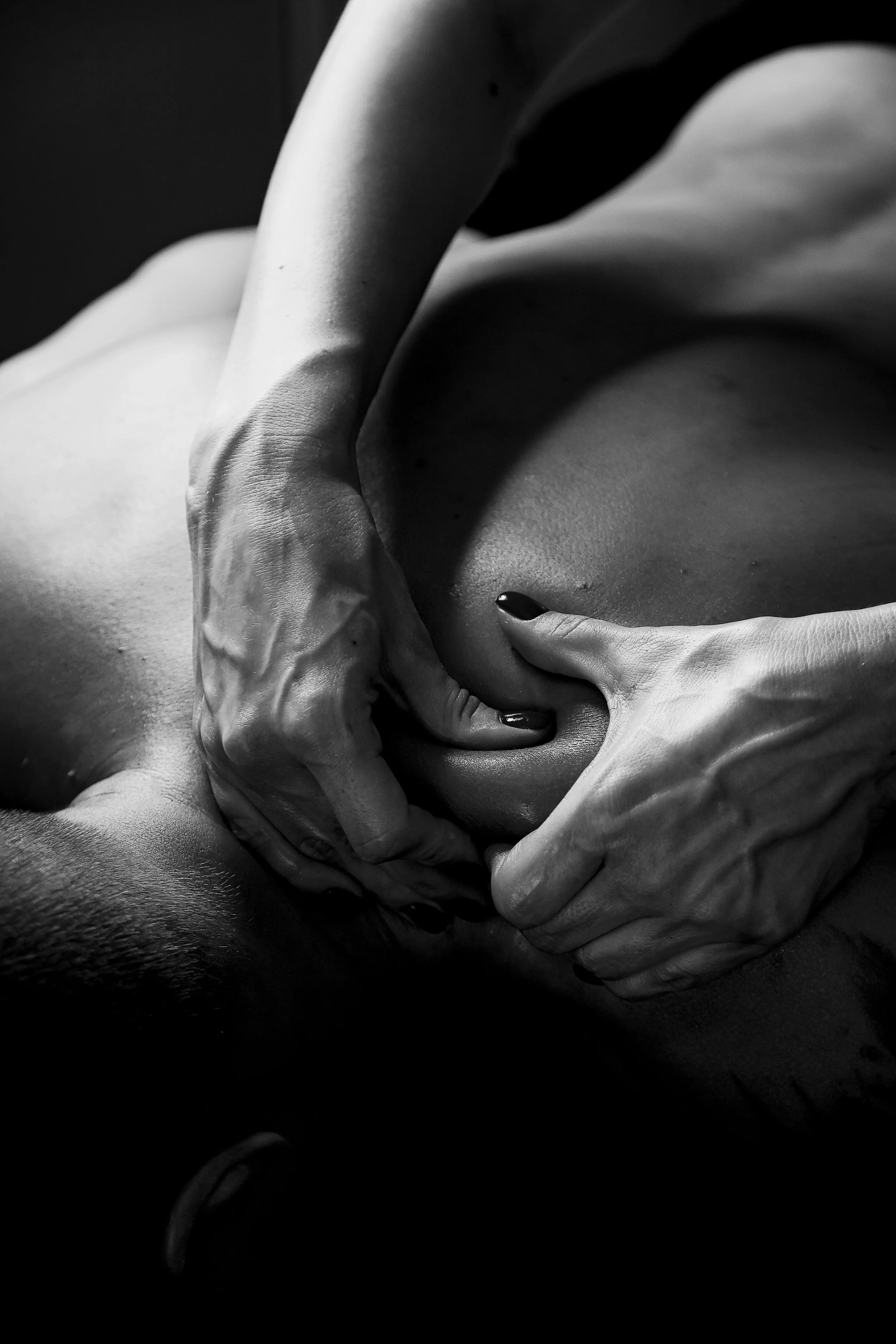 Black and white close-up of hands gently kneading a person's body in a massage or similar activity.