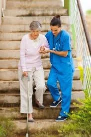 A caregiver assisting an elderly woman with walking on outdoor stairs