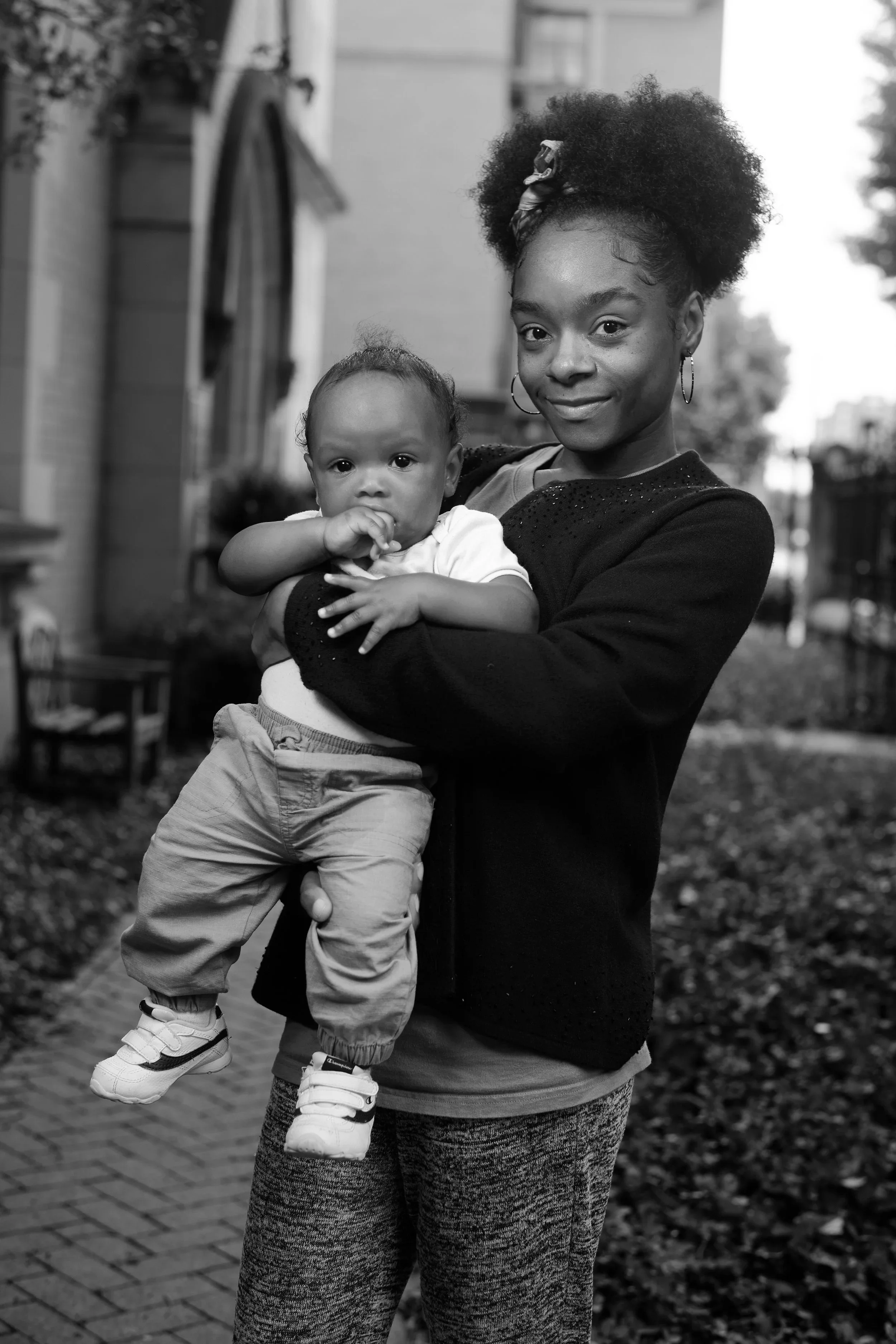 A woman holding a young child outdoors in a residential neighborhood.