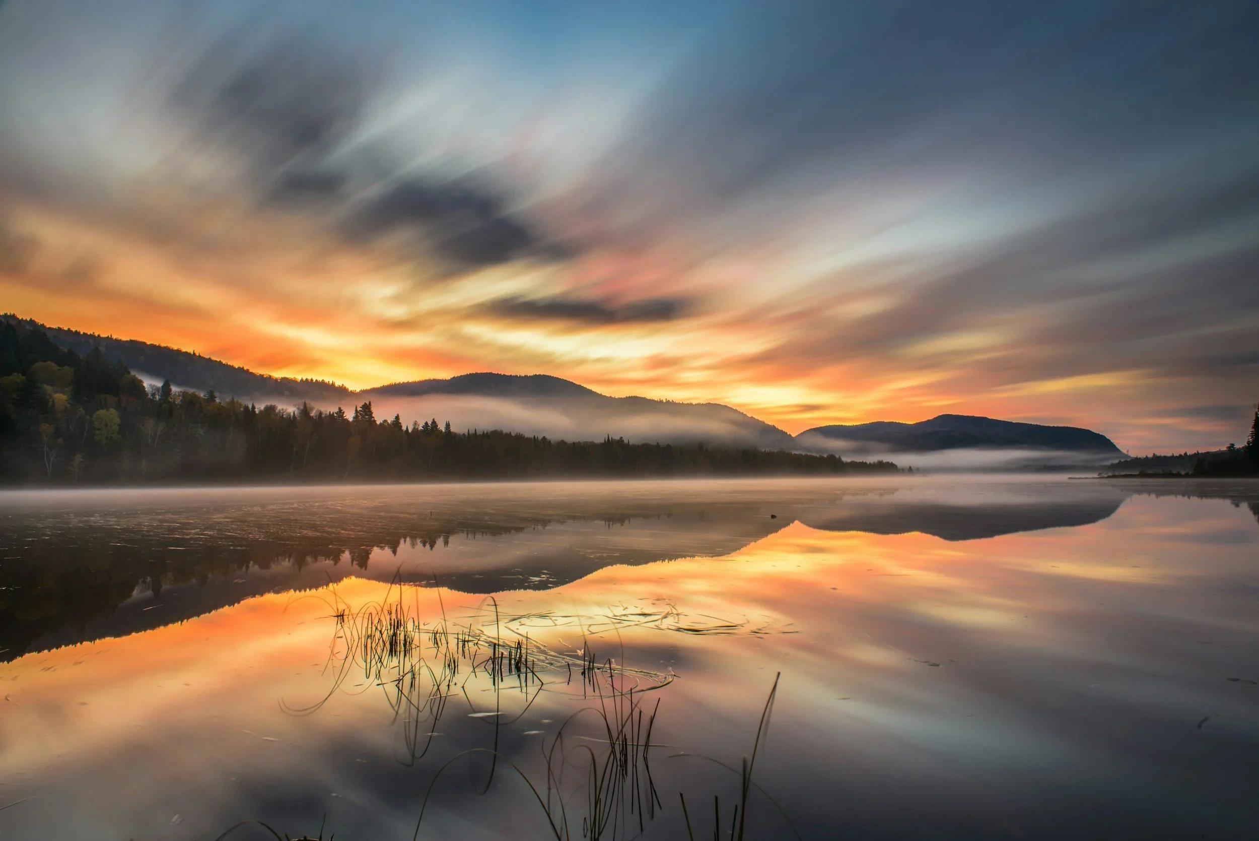 Sunrise over a calm lake with mountains in the background, mist on the water, and colorful clouds in the sky.