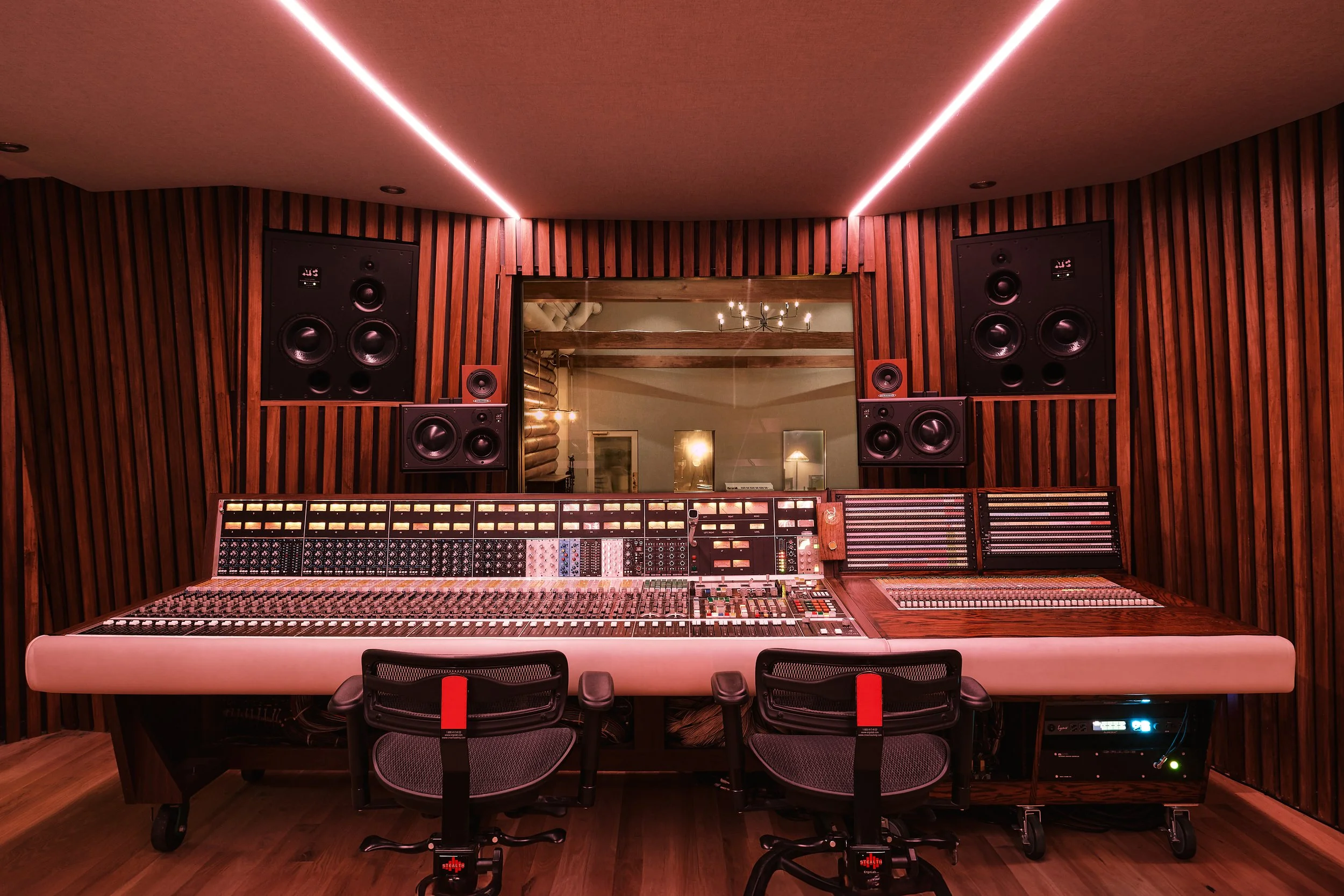 Recording studio with large mixing console, wooden wall panels, and multiple speakers.