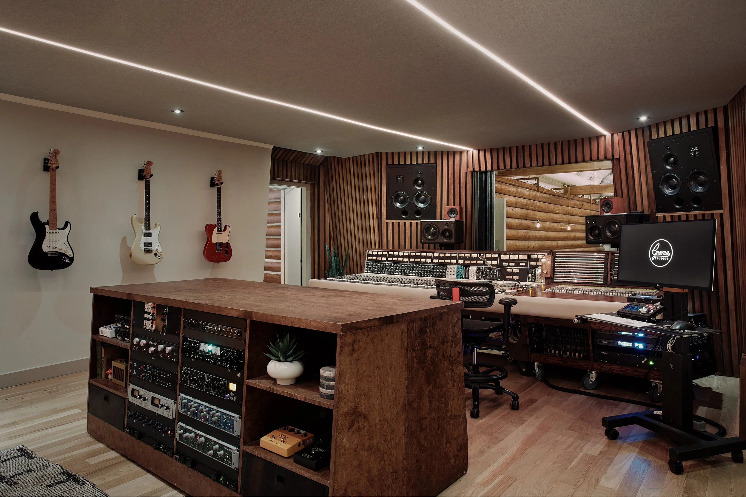 Music recording studio with guitars on the wall, large mixing console, studio monitors, computer, and various audio equipment.