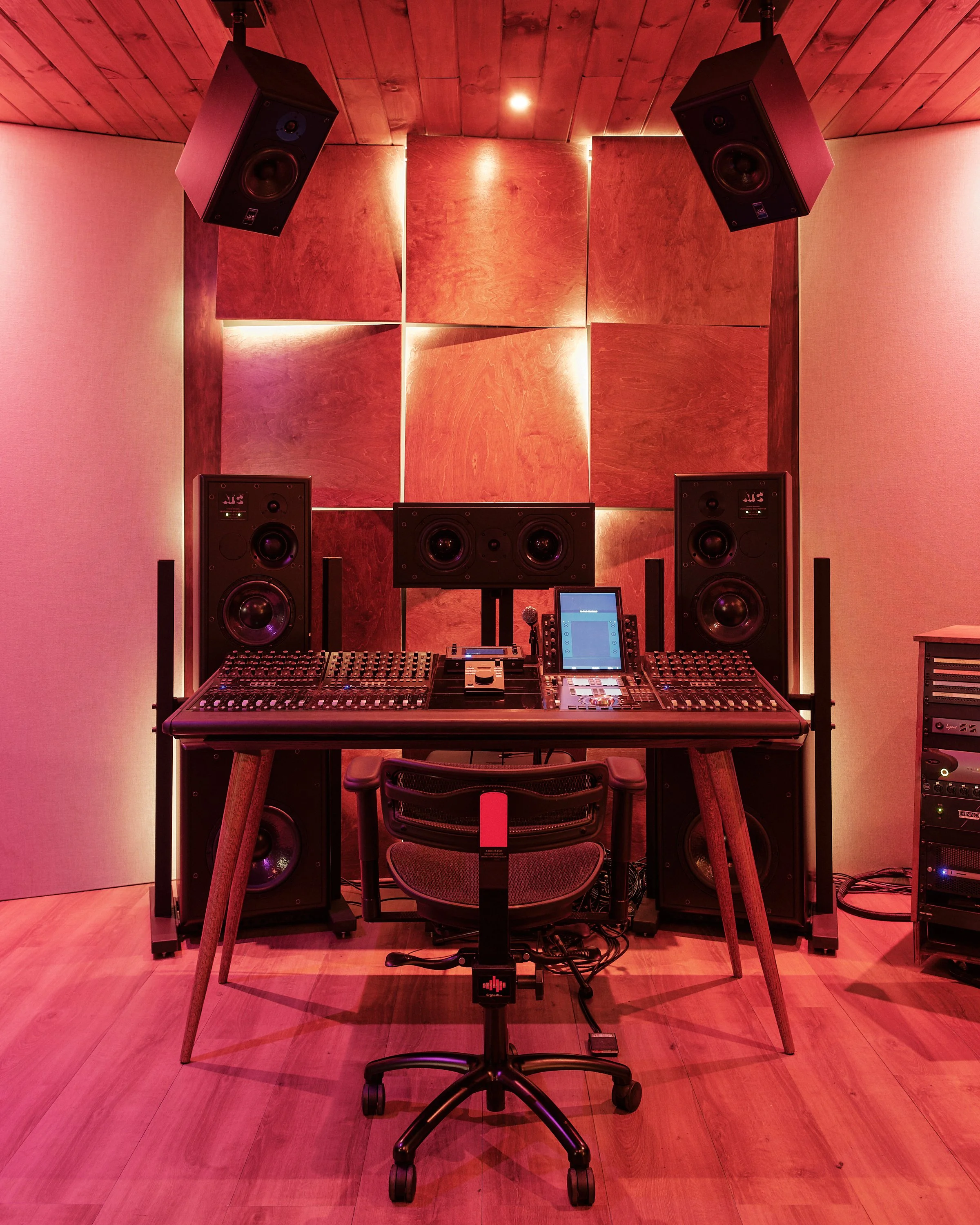 A professional recording studio with a mixing console, large speakers, a computer monitor, and acoustic panels on the walls, illuminated with warm lighting.