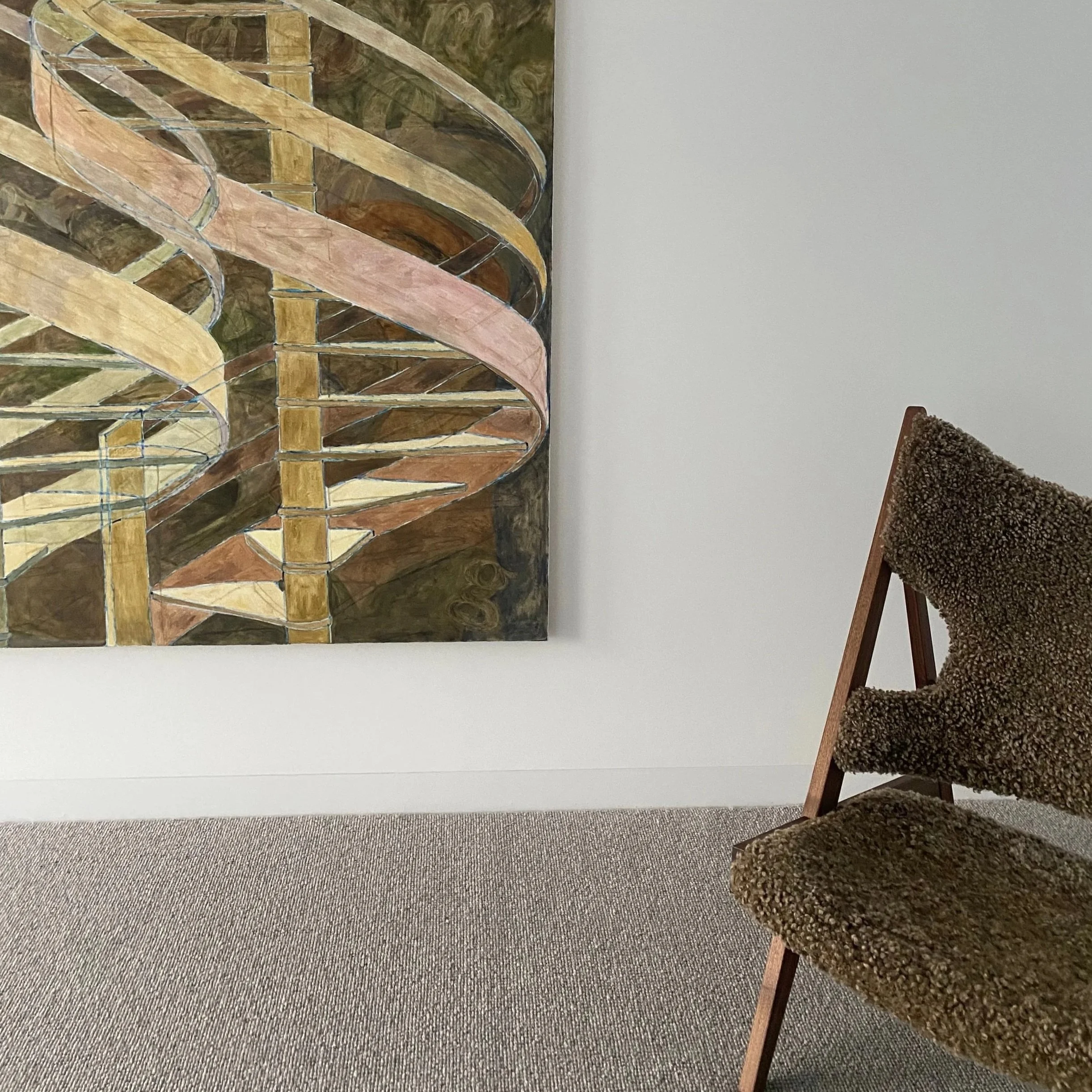 A framed painting of a wooden spiral staircase with curved handrails hangs on a white wall, next to a brown textured upholstered chair with a wooden frame, on a beige carpeted floor.
