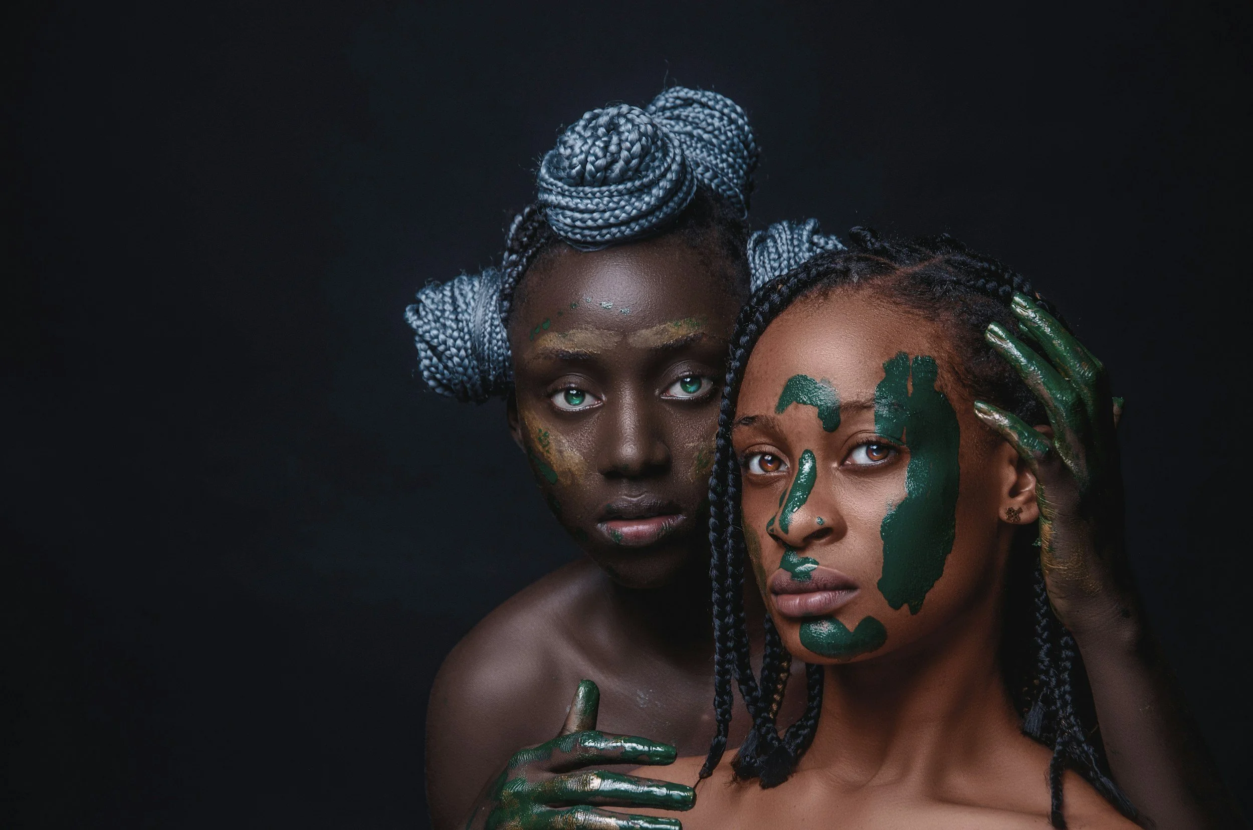 Two women with painted faces and braided hair posing against a dark background. ritual painting, ritual theatre