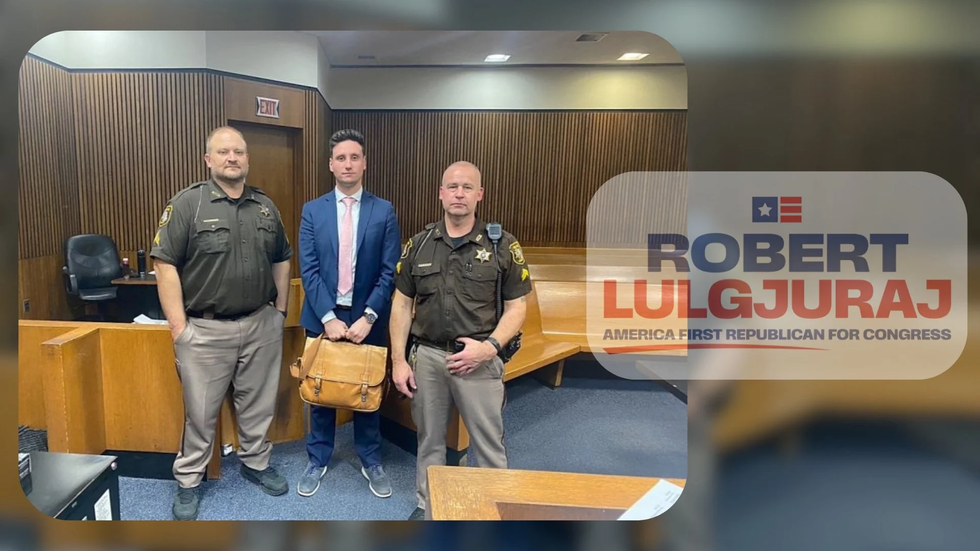 Three men standing inside a courtroom, two are police officers in uniform and one is in a suit and tie. There is a wooden judge's bench behind them.