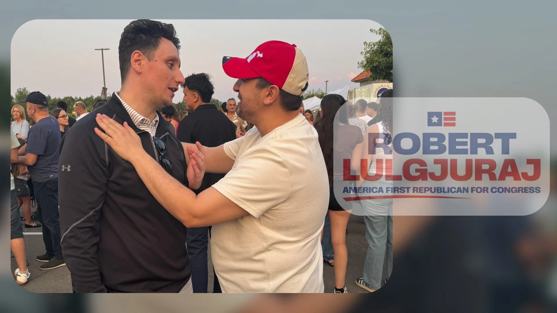 Two men are facing each other, holding each other's shoulders and chest, at an outdoor political event with a crowd in the background. One man is wearing a black Nike jacket, and the other is wearing a white shirt and a red cap. There is a campaign s