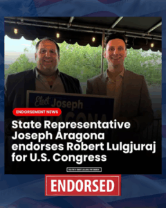 Two men in suits at an outdoor event, one of them is holding an endorsement sign, with a headline about State Representative Joseph Aragon endorsing Robert Lulguruaj for U.S. Congress.