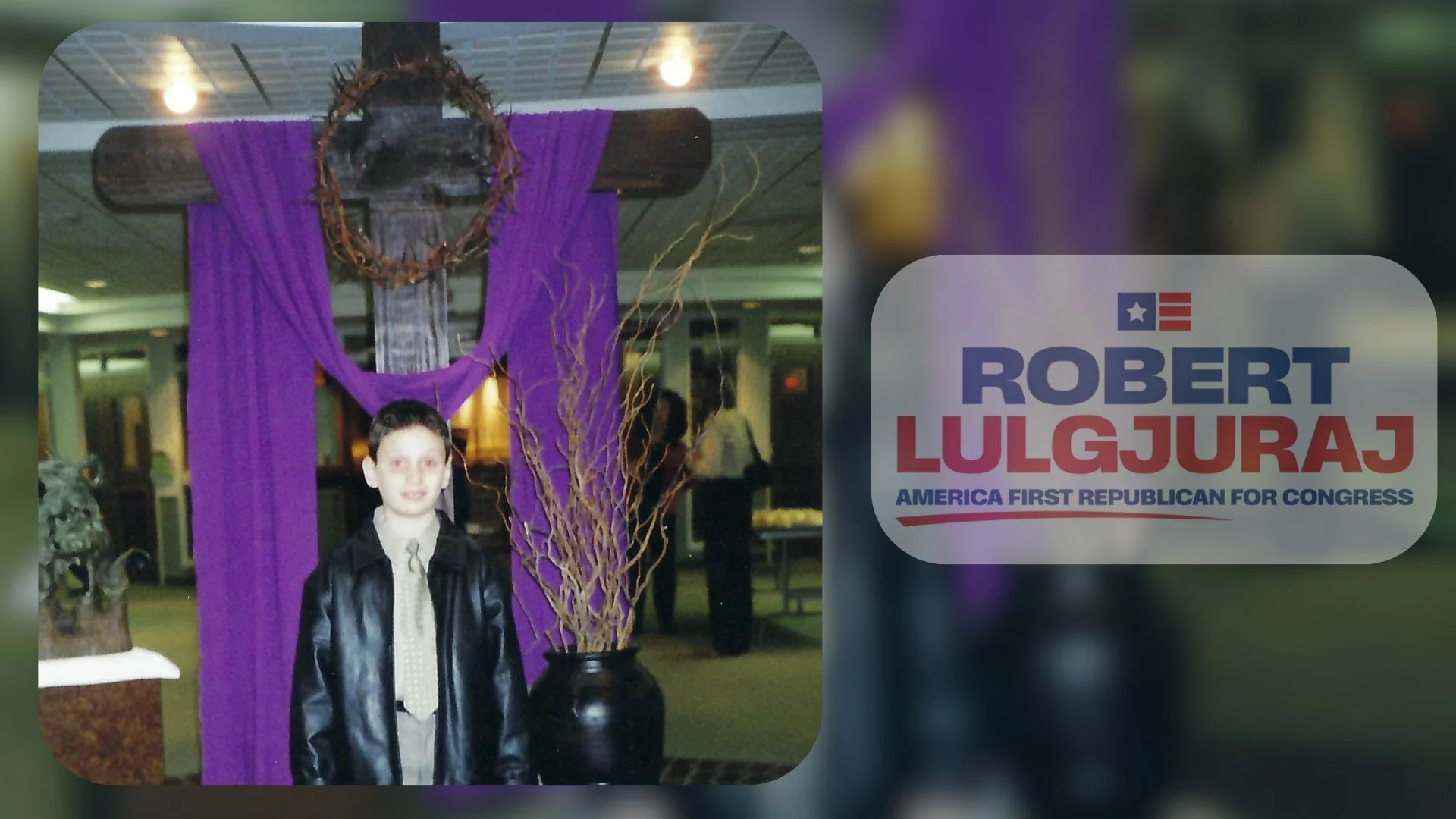 A young boy in a leather jacket and light-colored shirt with a tie standing in front of a large wooden cross draped with purple cloth and decorated with a wreath. The setting appears to be indoors with people in the background. To the right, there is