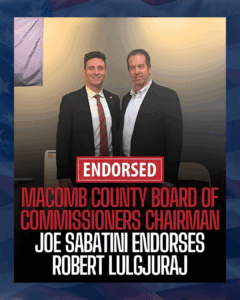 Two men in suits standing together, one with a red tie. The image features text that says 'ENDORSED MACOMB COUNTY BOARD OF COMMISSIONERS CHAIRMAN' and 'JOE SABATINI ENDORSES ROBERT LULGURAJ'.