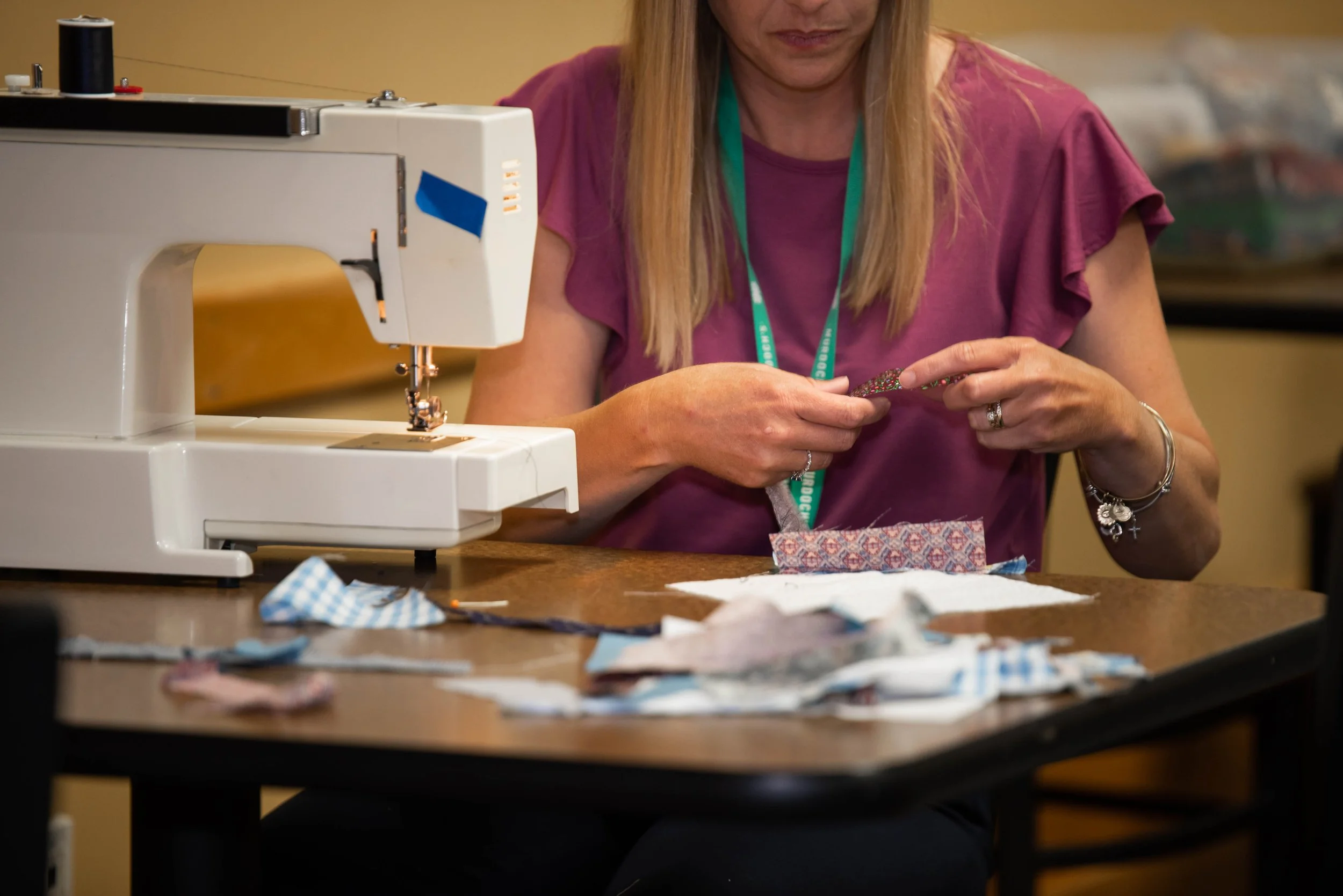 A woman sewing fabric pieces with a sewing machine on a wooden table.