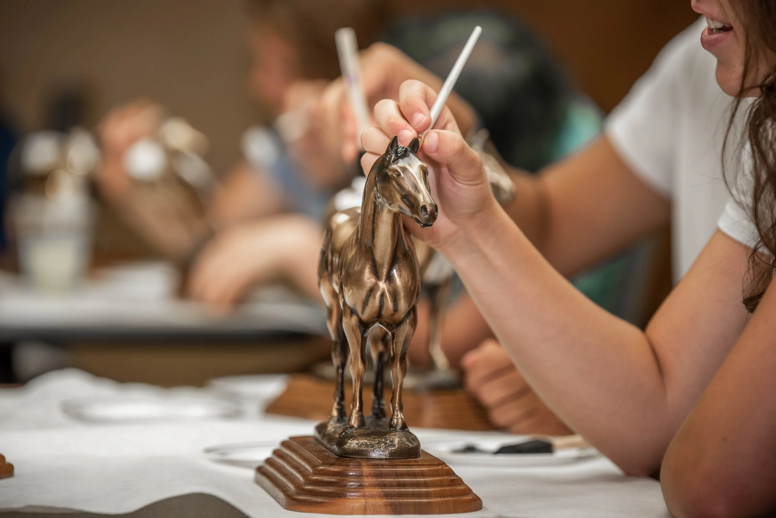Person painting a bronze horse sculpture at an art class or workshop.