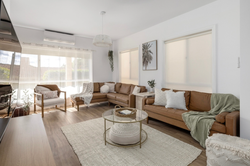 Bright living room with white walls, brown couch, white green throw pillows, round glass coffee table, a light-colored rug, large windows with sheer curtains. Family friendly luxury accommodation, Port Stephens, Corlette, Nelson Bay, holiday home.