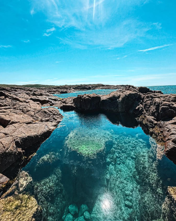 Rocky coastline with clear tidal rock pool reflecting the blue sky, with the ocean in the background under a partly cloudy sky on a sunny day. Nelson Bay, Port Stephens, Illawarra, Mollymook, Jervis Bay, NSW South Coast, Boat Harbour