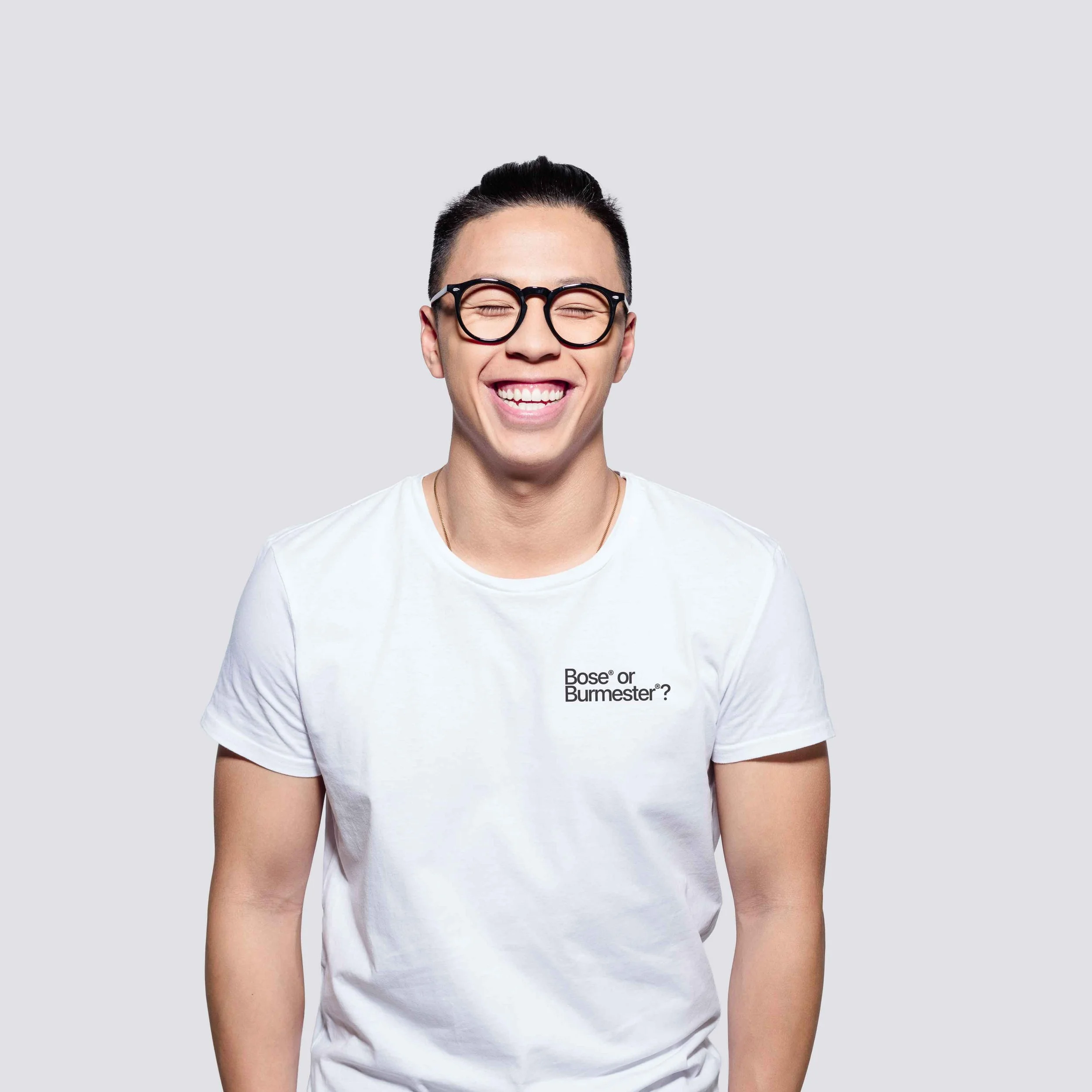 A smiling Porsche enthusiast with glasses and a white t-shirt with text that asks 'Bose or Burmester?'