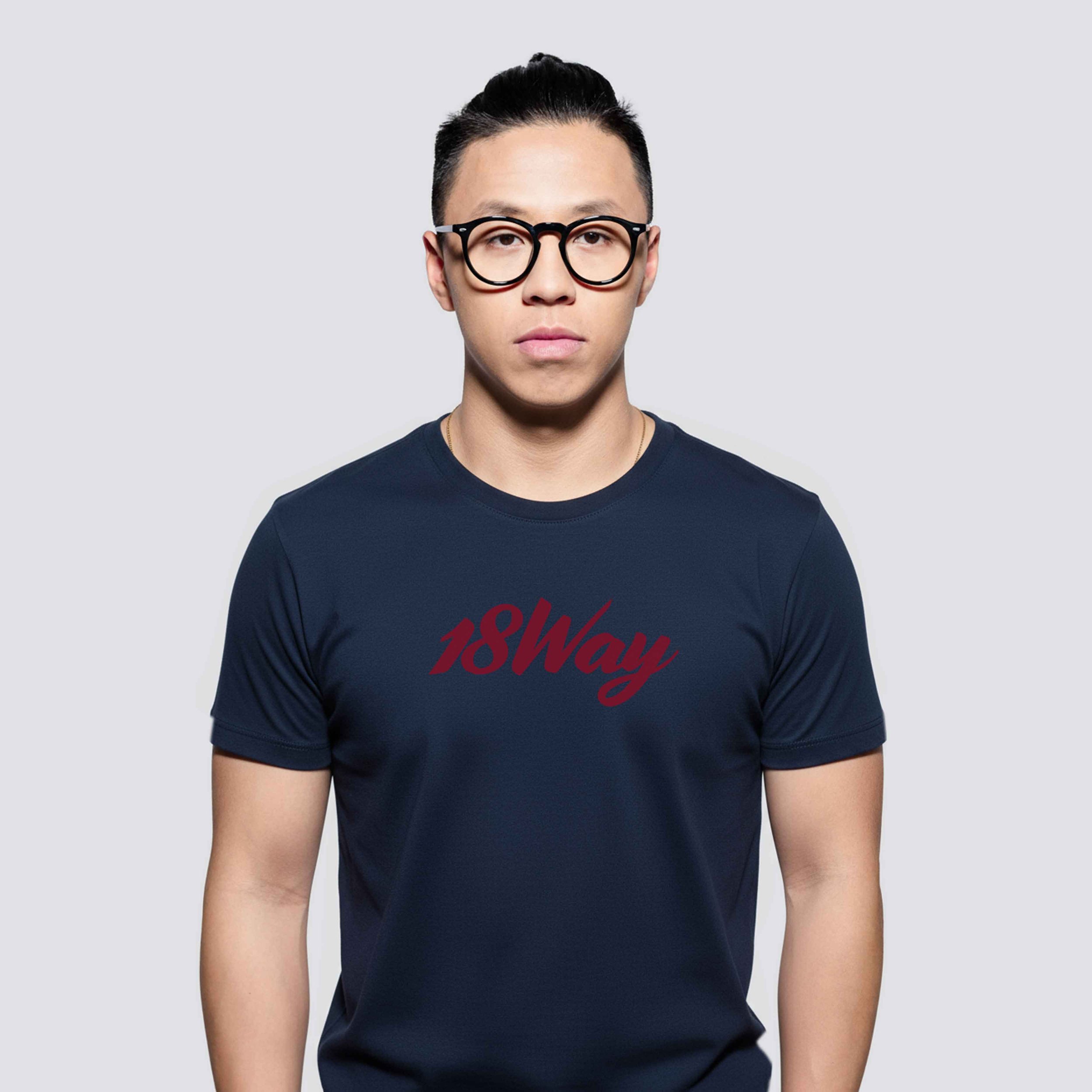 Young man with glasses wearing a navy blue t-shirt with red text '18Way' printed on it, standing against a plain gray background.