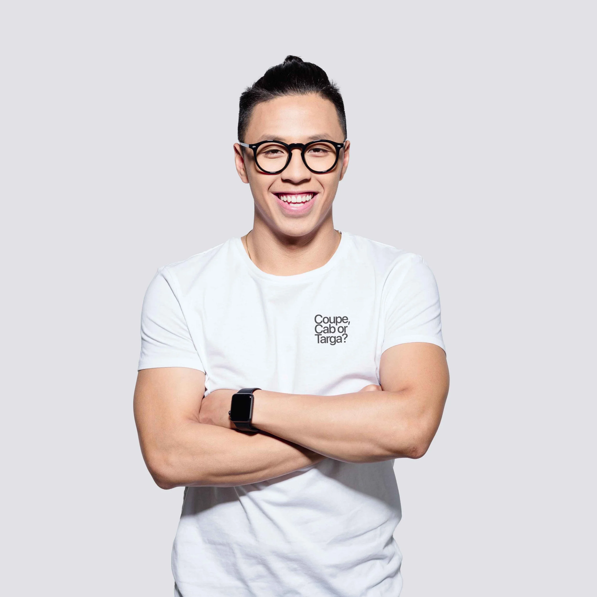 Smiling Porsche enthusiast with glasses and smartwatch wearing a white 18Way T-shirt with text and crossing arms pose.