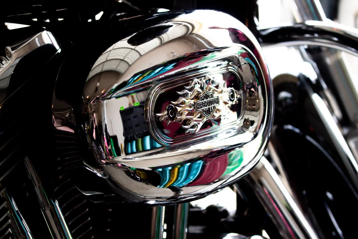 Close-up of a Harley-Davidson motorcycle engine with a shiny chrome cover and logo, reflecting surrounding colors and objects.