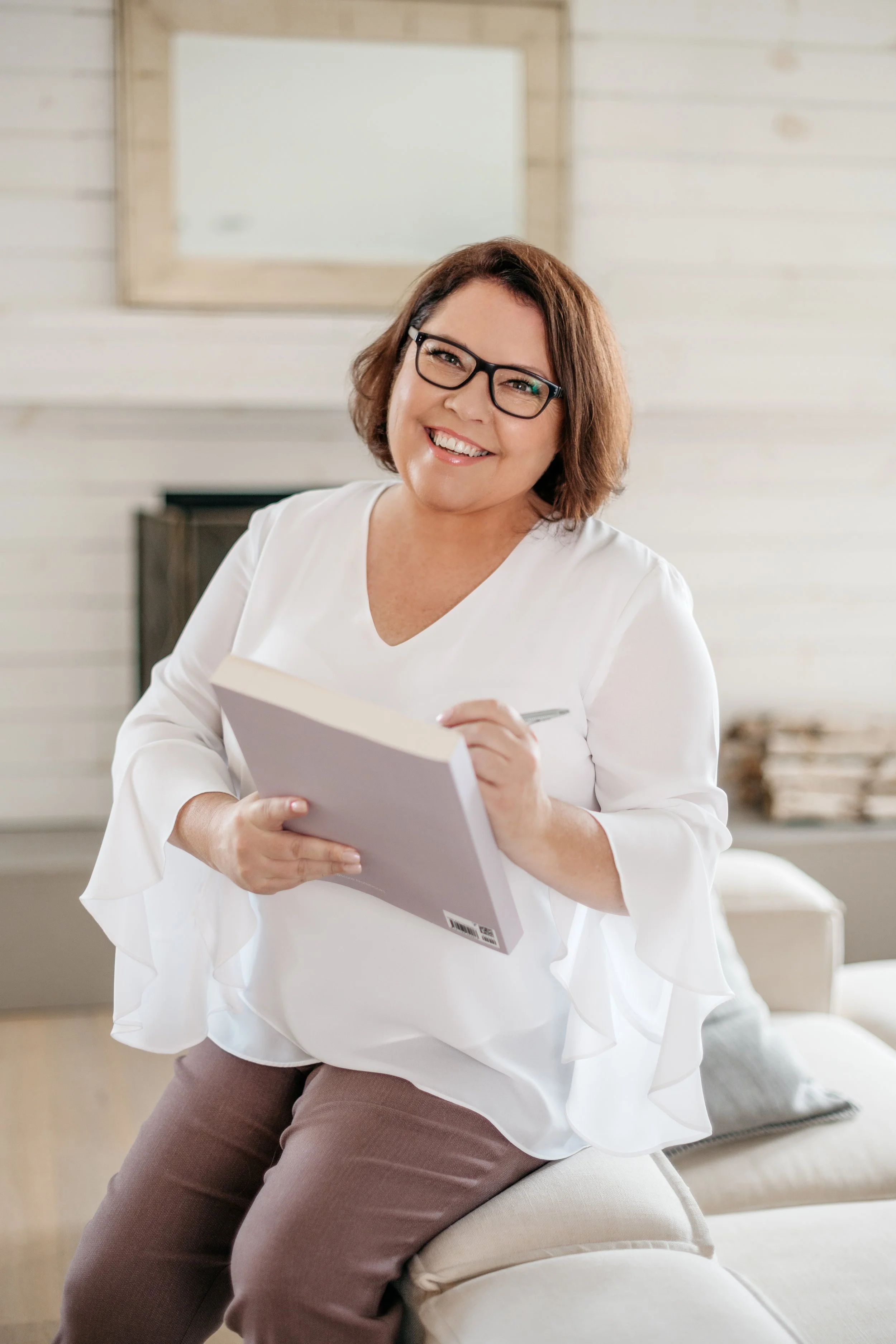 Shannon Hazel holding a notebook and pen, sitting on a couch in a cozy, well-lit room.