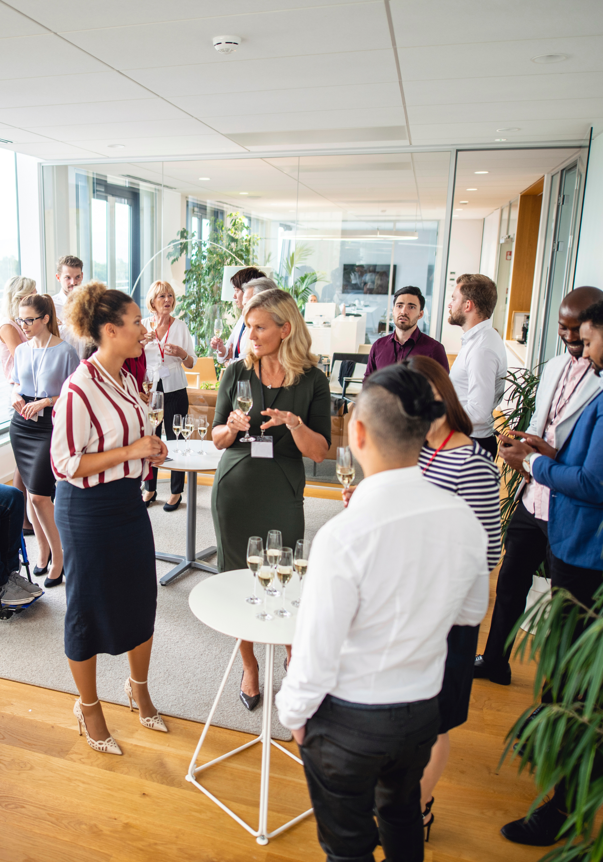 Business professionals at a networking event in a modern office, holding wine glasses and engaging in conversations.