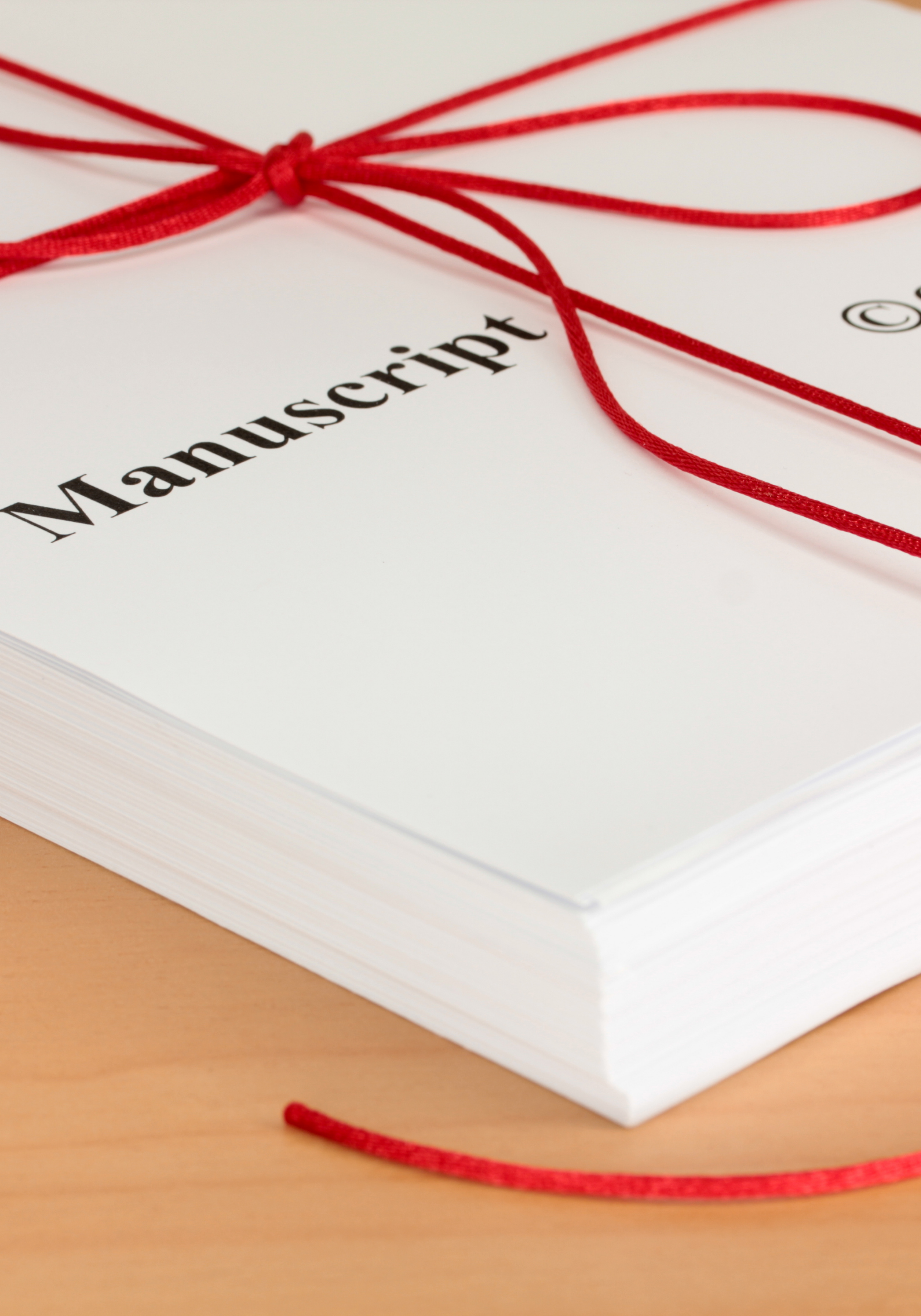 Close-up of a stack of white manuscript pages tied with a red string, with the word 'Manuscript' printed on the top page.