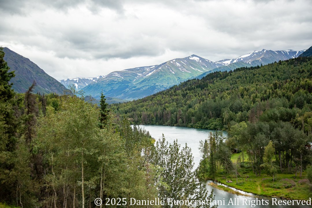 Wide landscape view of the Kenai River winding through forested valley with mountains in the background in Alaska.