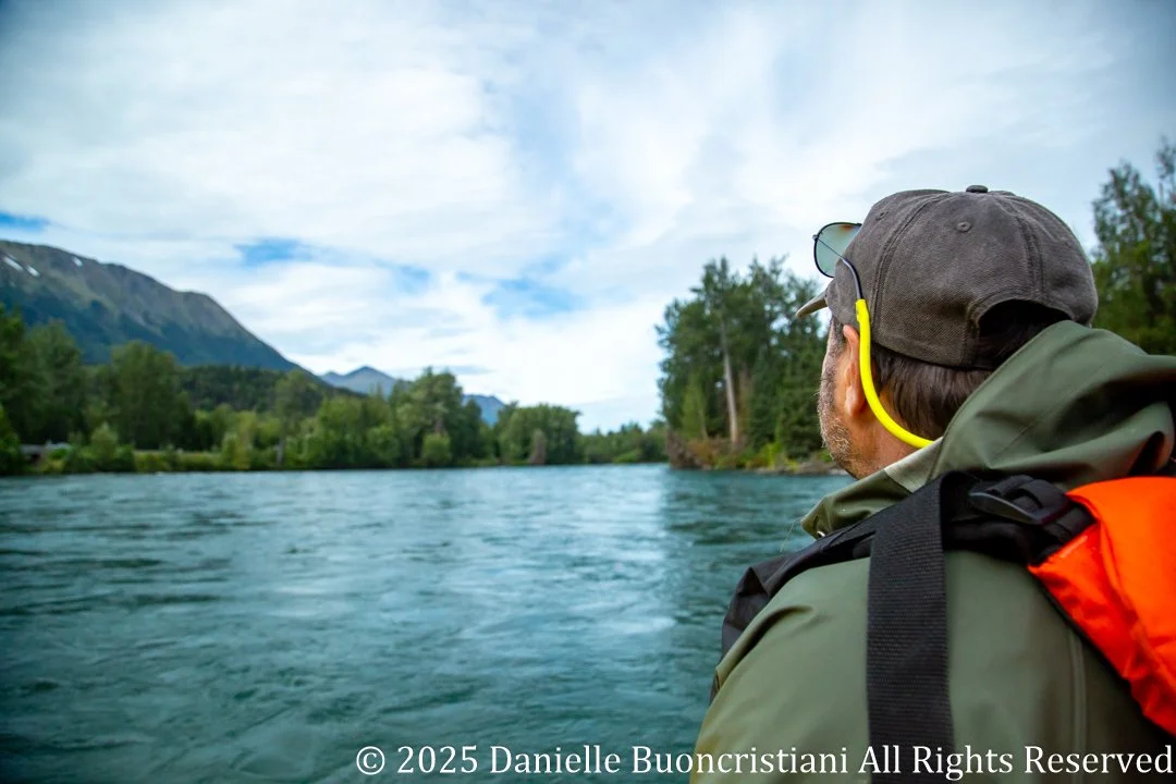 Man in a raft looking out over the turquoise Kenai River with mountains and forest in the background in Alaska.