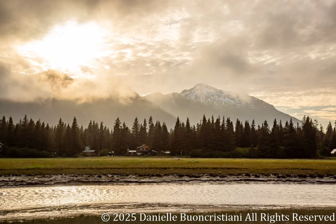 Silver Salmon Creek Lodge beneath misty Alaskan mountains with soft, filtered light, reflecting calm and stillness after a storm.
