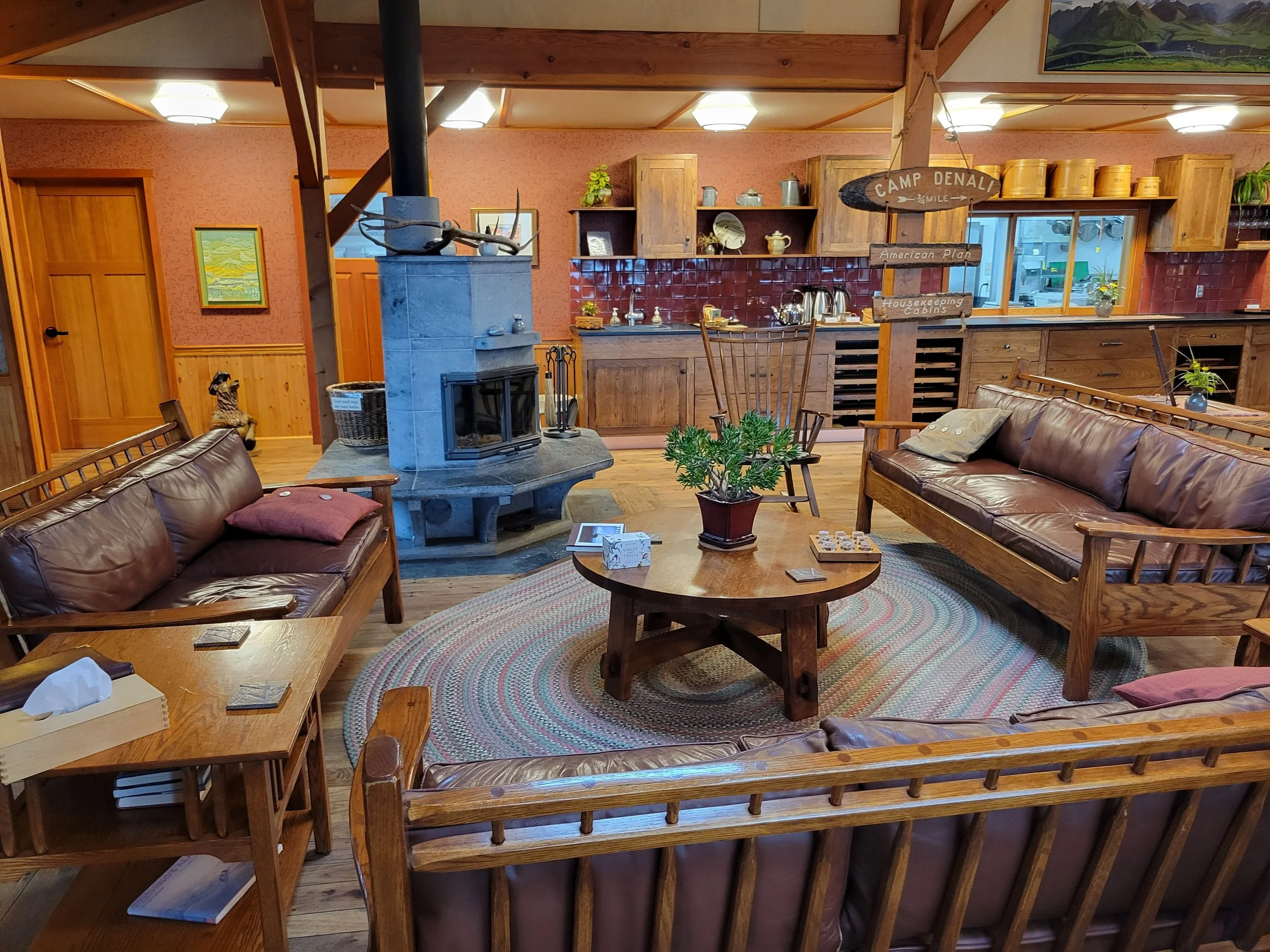 Warm lodge interior at Camp Denali with wood furniture, leather couches, and a central wood stove gathering area.
