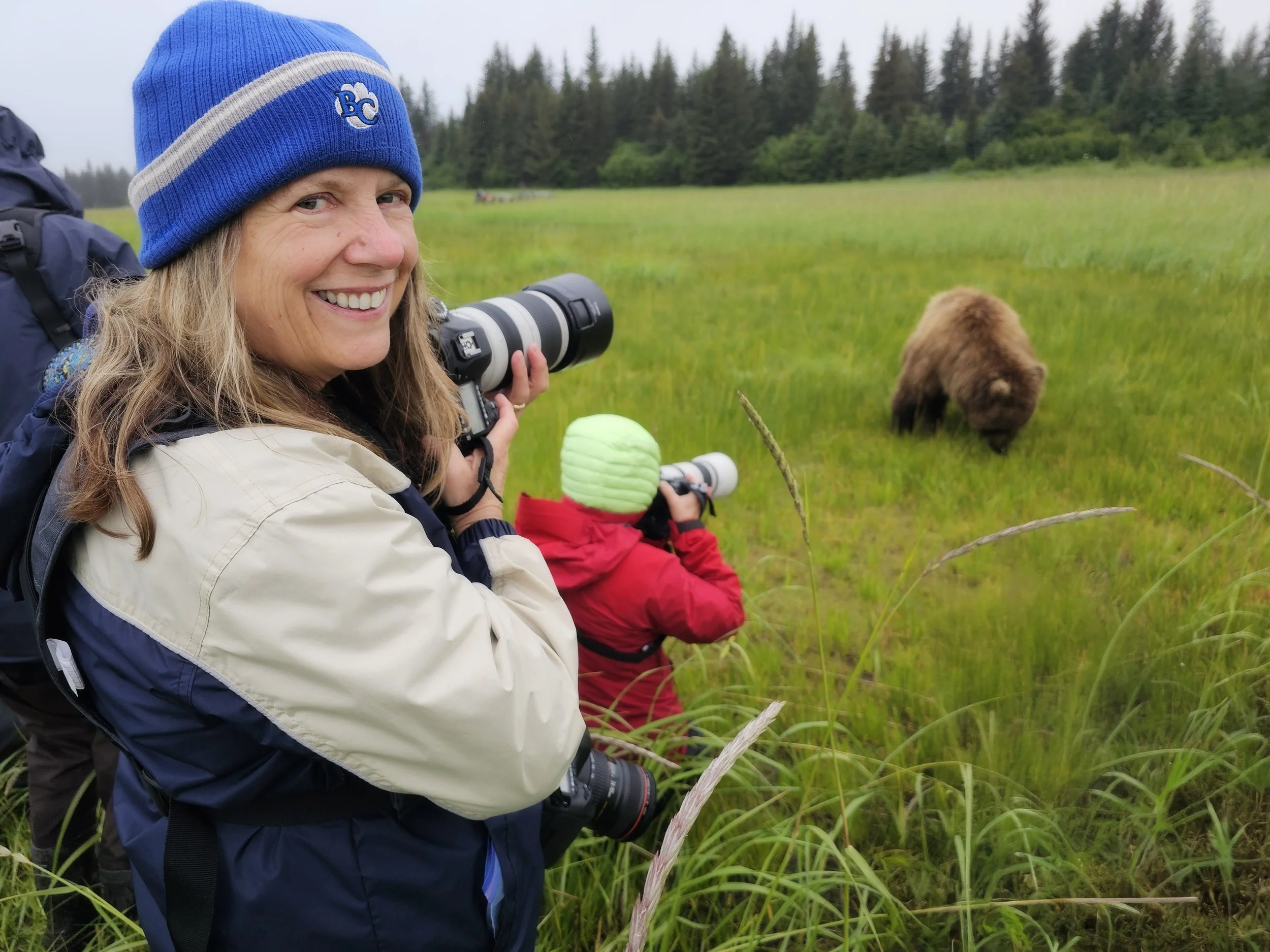 Photographer Danielle Buoncristiani standing in a meadow with coastal brown bears nearby at Lake Clark