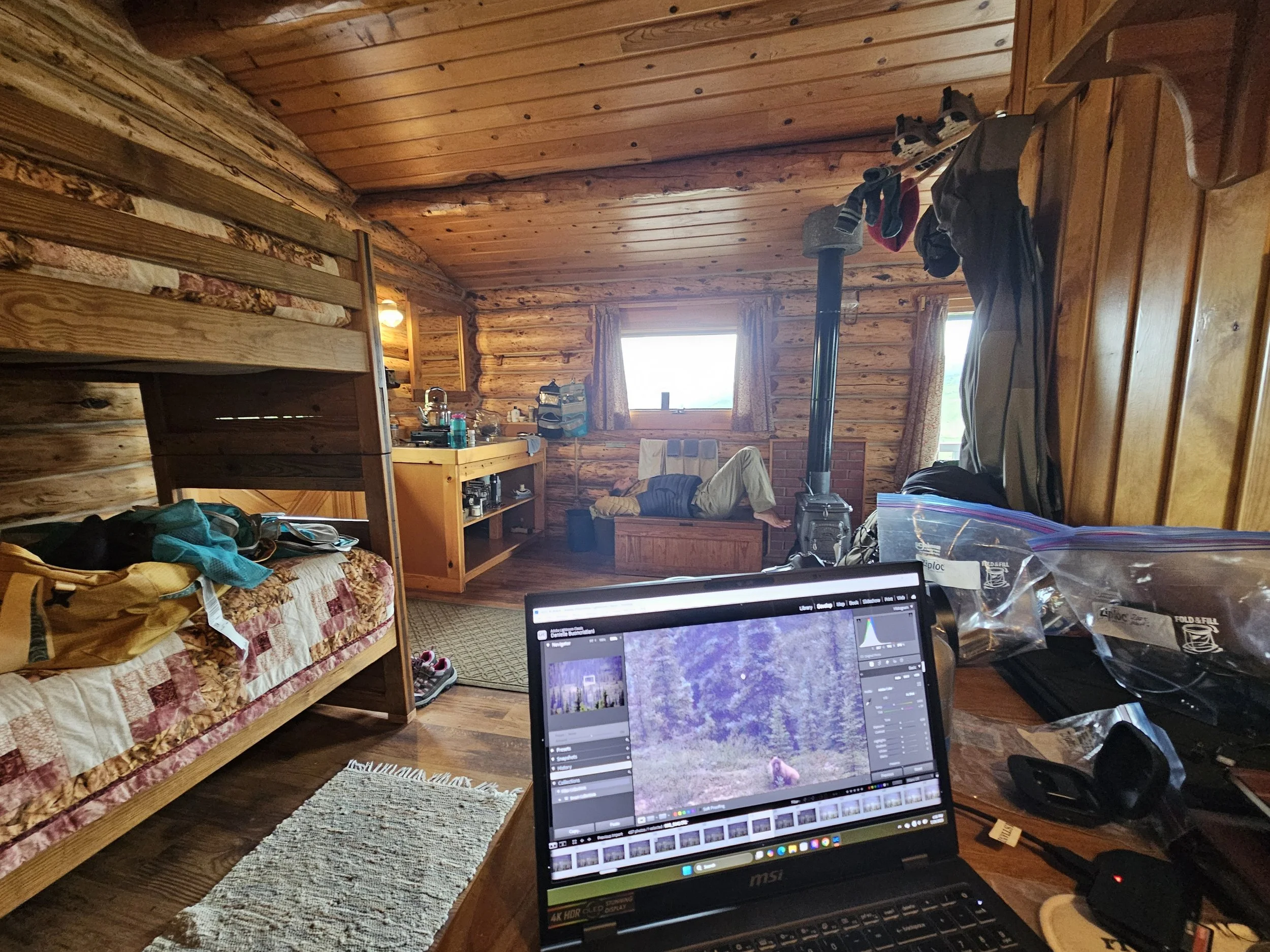 Interior of a Camp Denali cabin with bunk beds, photography equipment, and a laptop editing wildlife photographs.