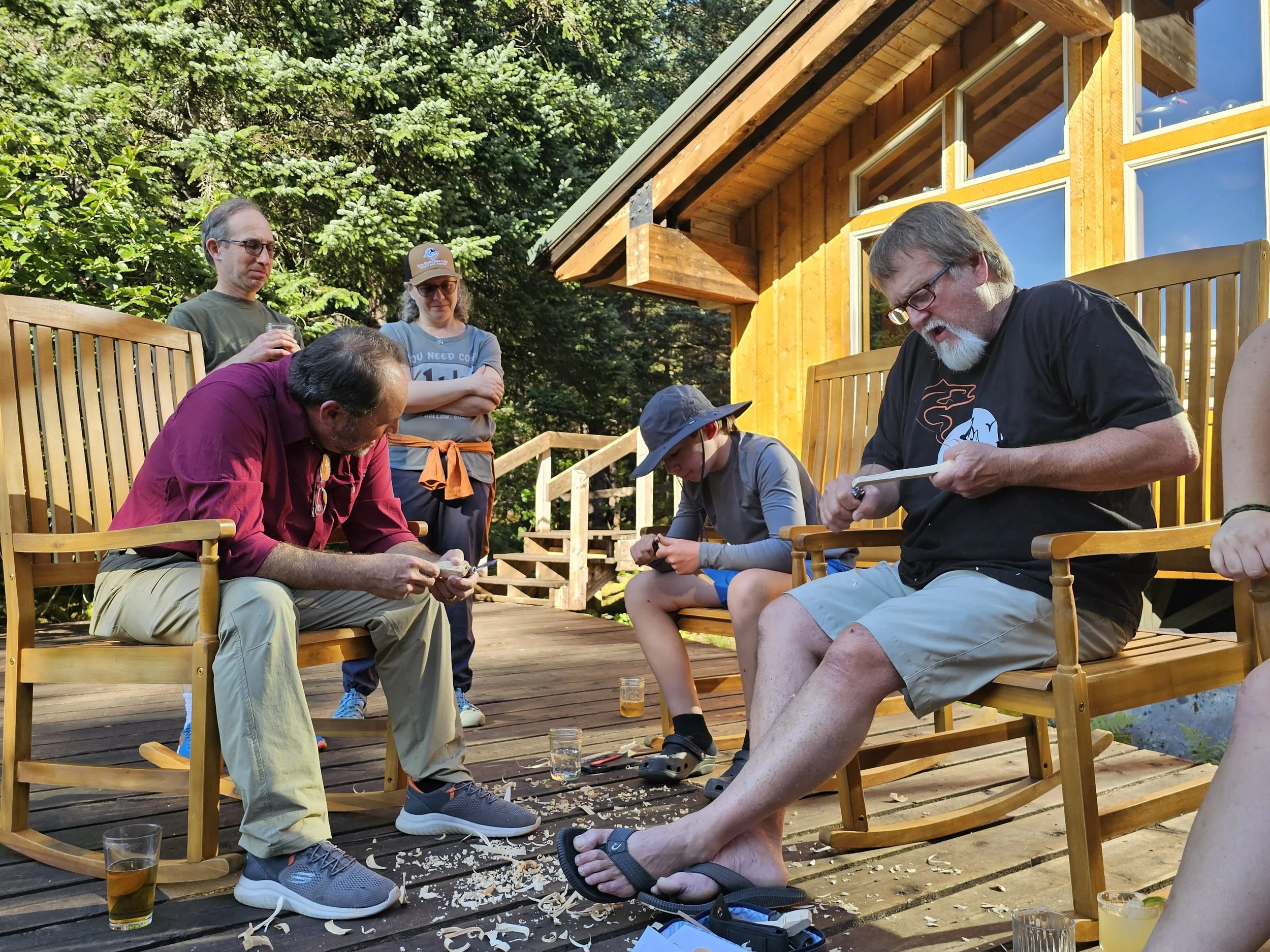 Group gathered on the deck of Kenai Fjords Glacier Lodge learning traditional wood carving in the evening light.