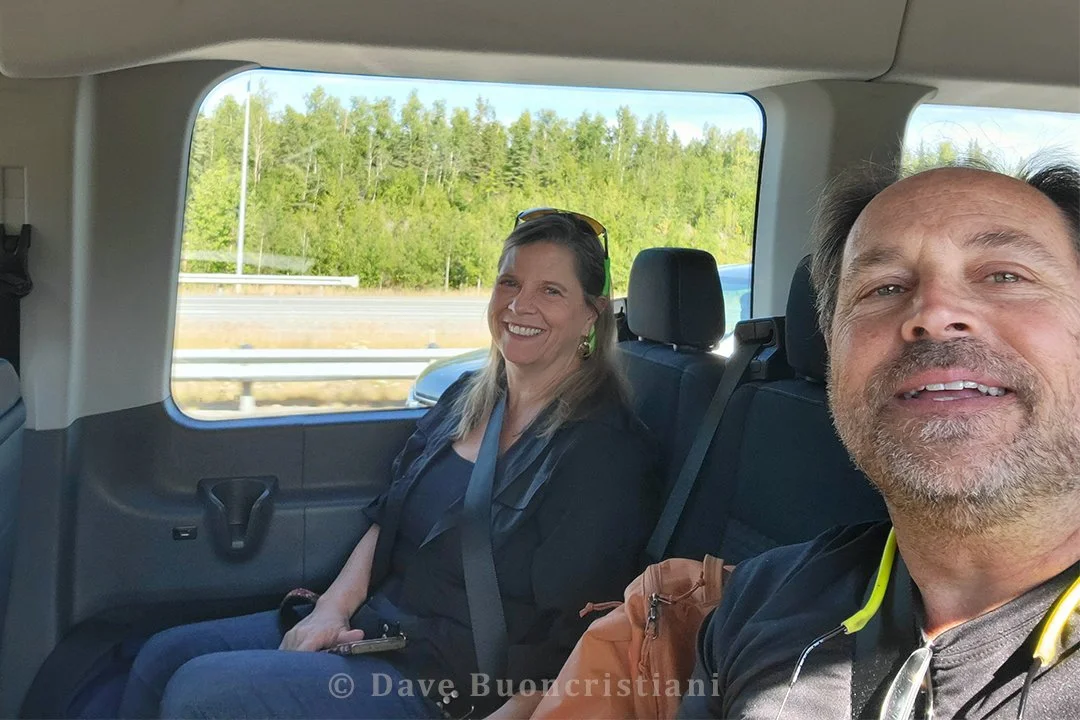 View inside a passenger van with travelers seated and forest visible through the window during the drive toward Denali National Park.