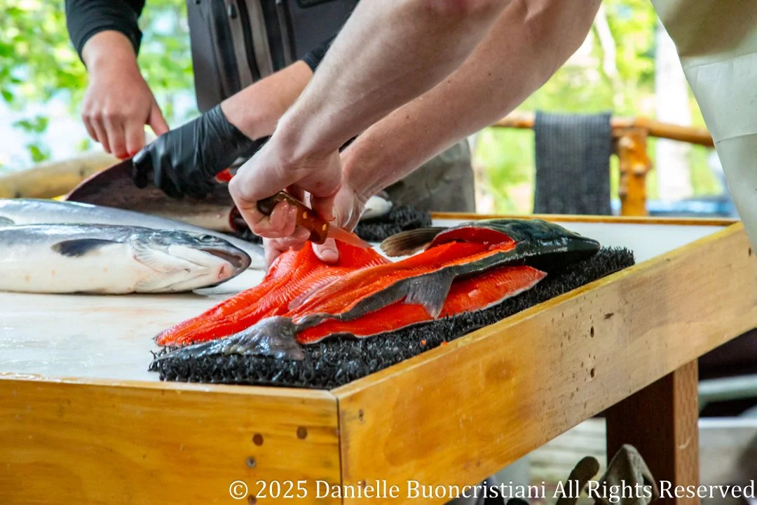 Hands filleting bright red salmon on a wooden table at Kenai Riverside Lodge in Alaska.