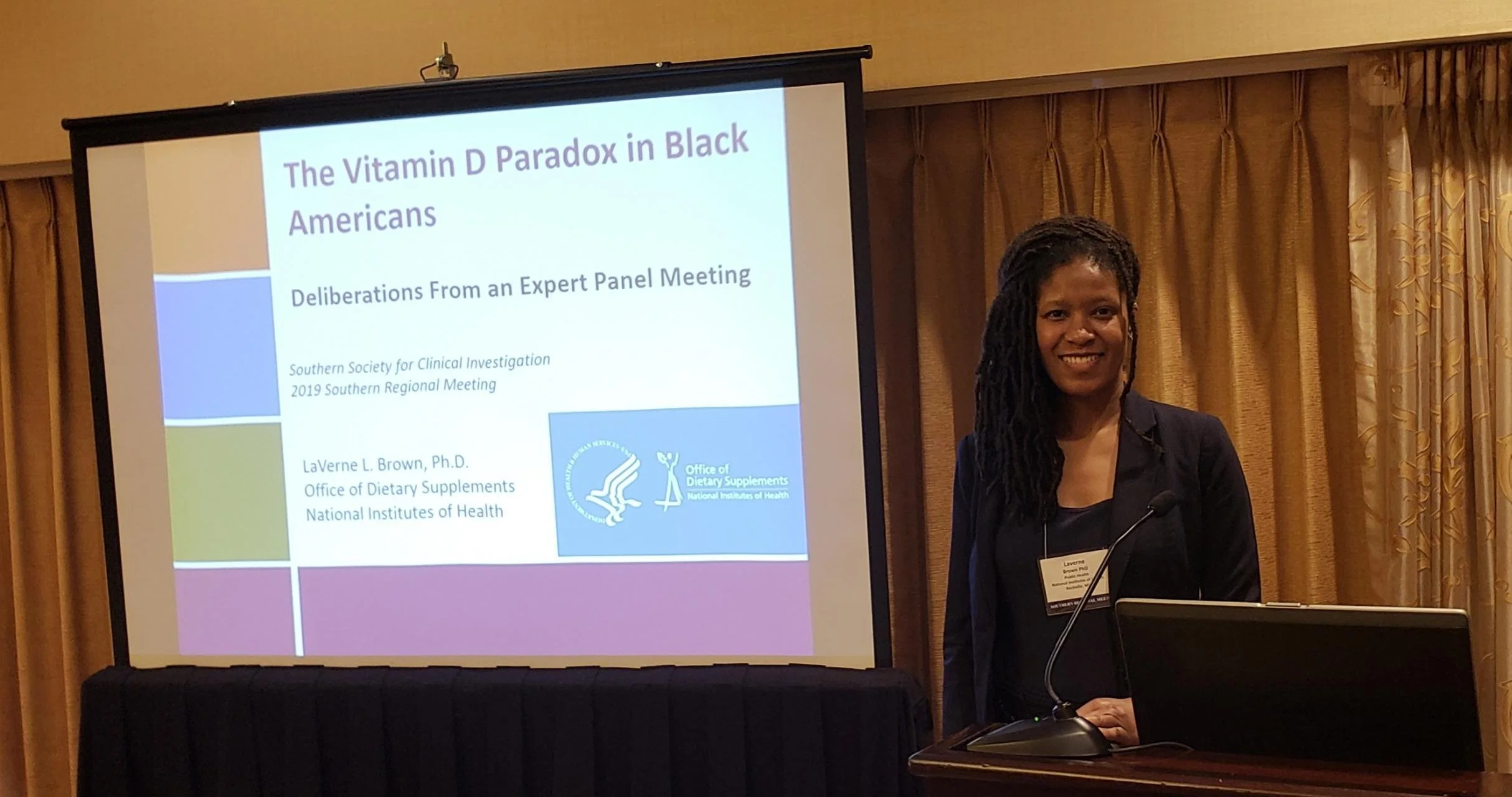 Woman standing at a podium with a presentation slide behind her at a conference.