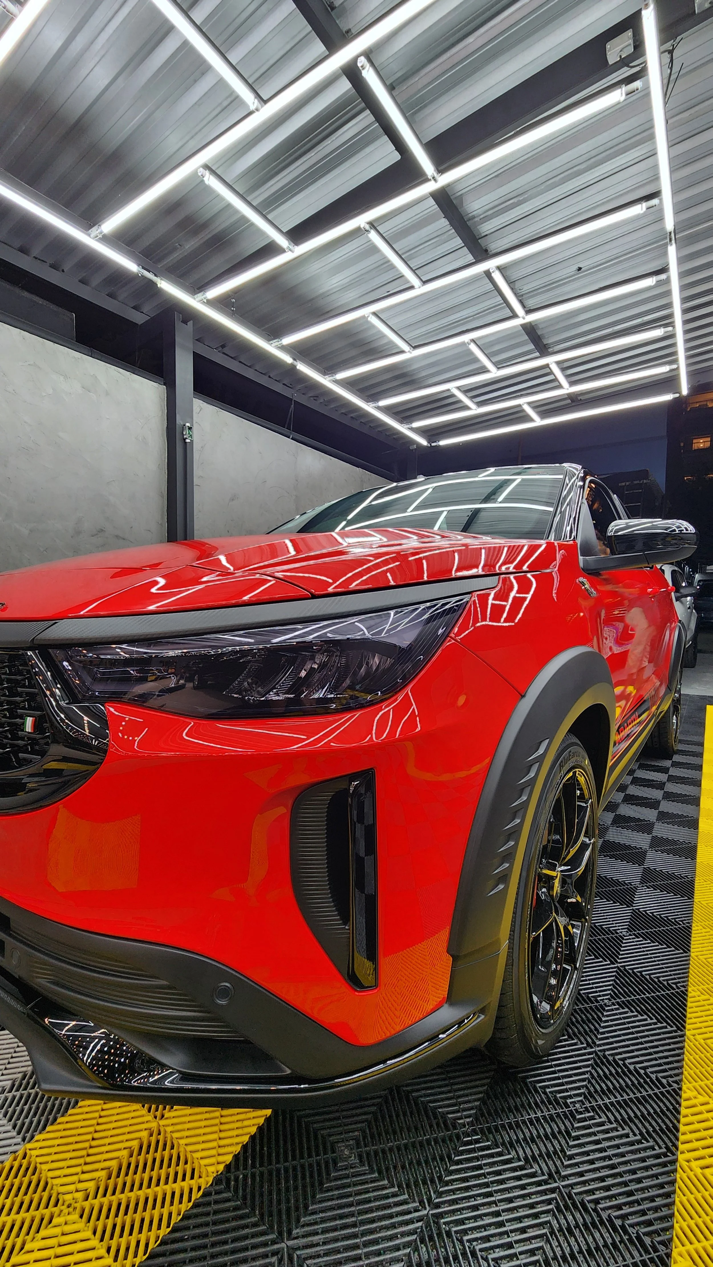 Carro esportivo vermelho com detalhes pretos, estacionado em ambiente de showroom com iluminação moderna.