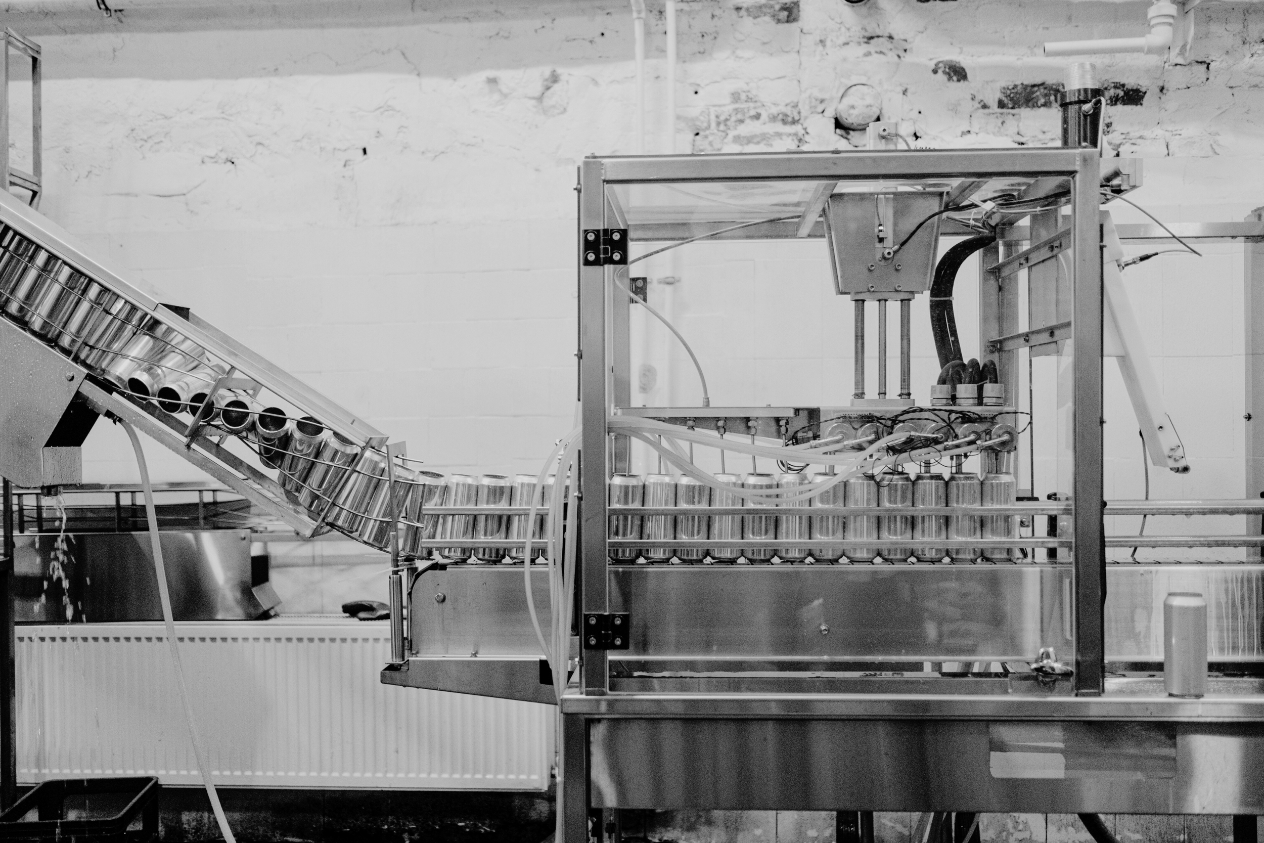 Industrial machinery with metal tanks arranged in a row and connected by tubes, possibly for filling or processing liquids, set against a textured brick wall in a factory or laboratory.