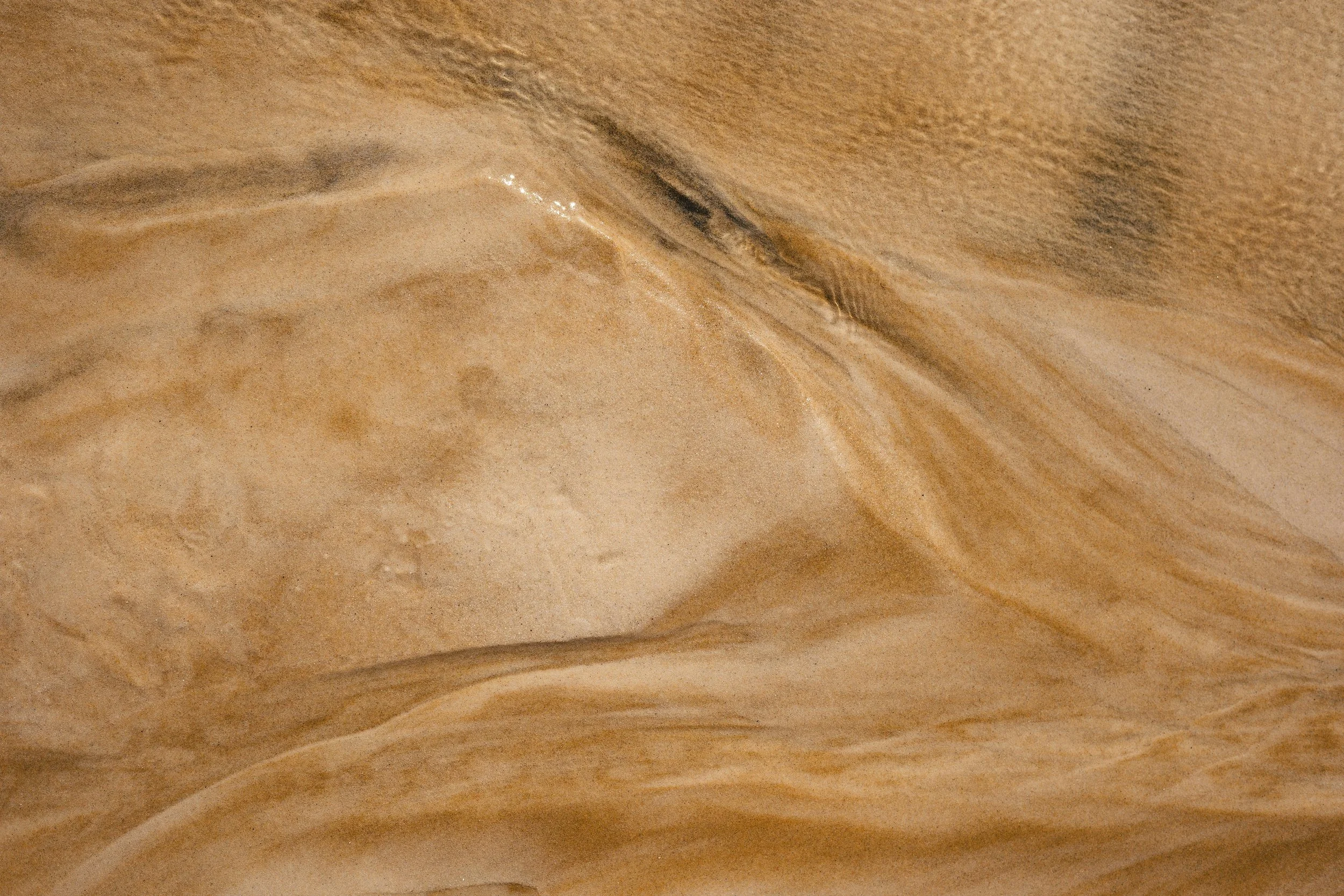 Close-up view of beige and brown layered marble or stone surface with smooth textures and natural patterns.