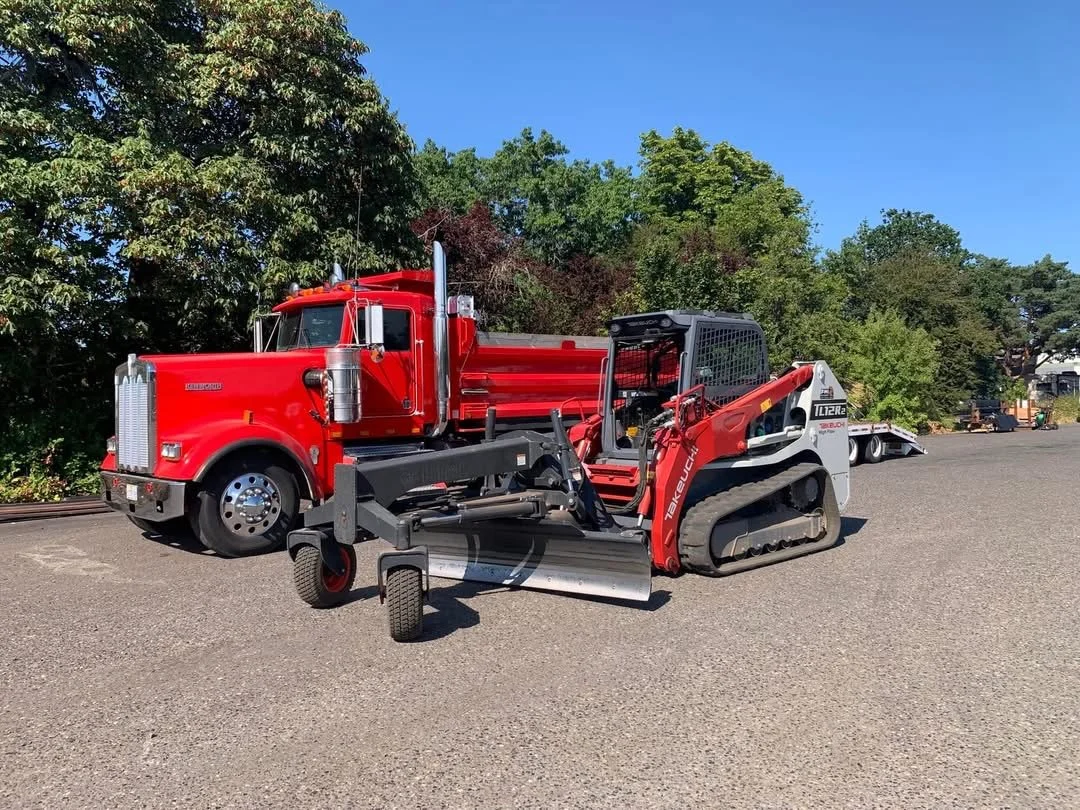 A red fire truck and a compact skid-steer loader parked on a paved surface with green trees in the background.
