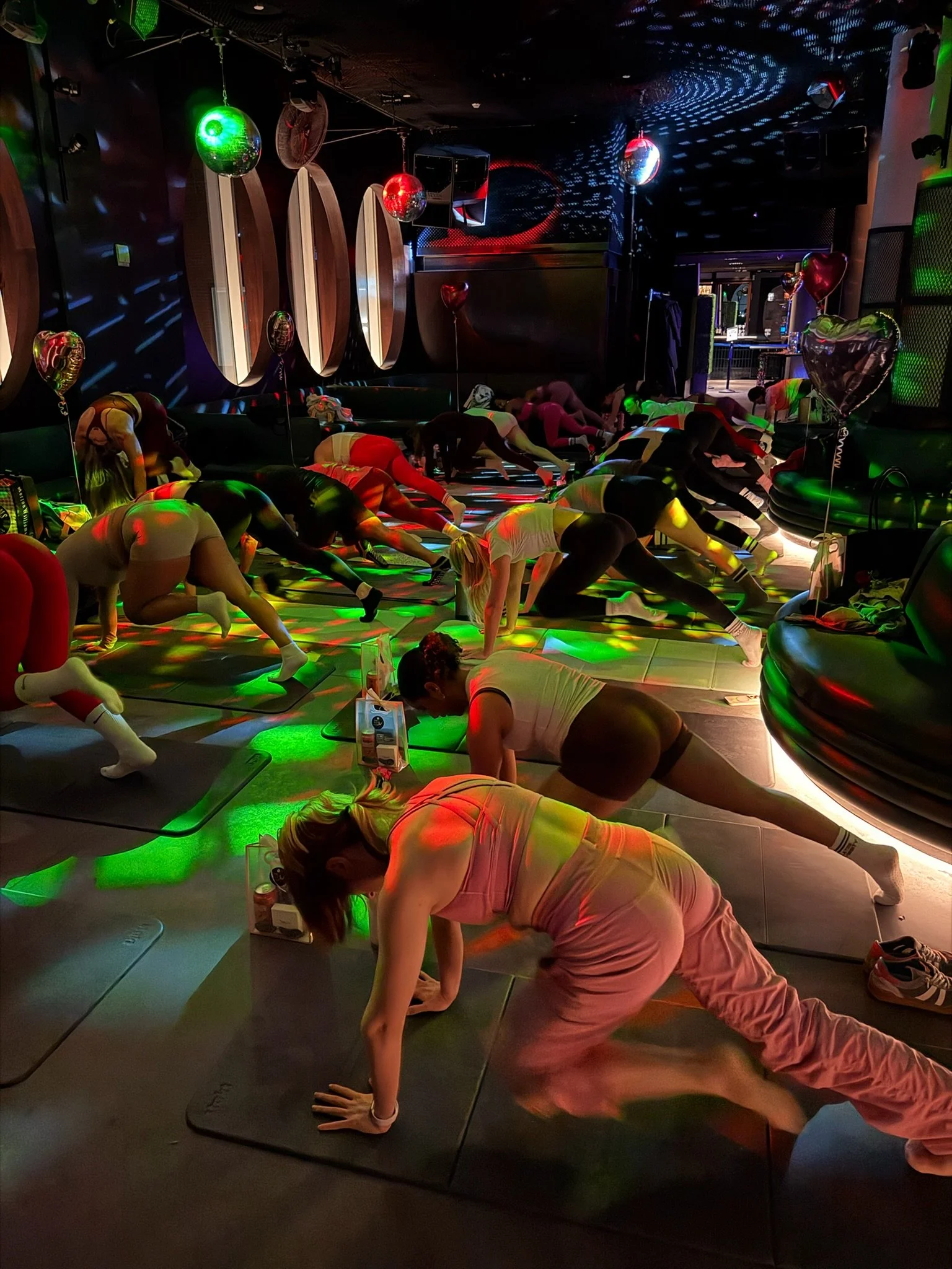 A group of people doing yoga on mats in a dark, colorful room with disco balls and stage lighting.