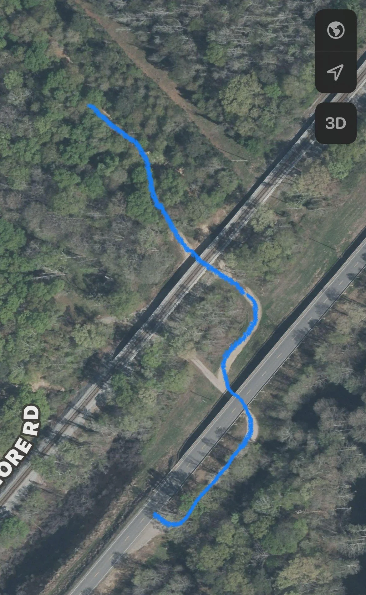 Aerial view of a winding blue trail running through a wooded park area next to a railway track and a road labeled 'More Rd'.