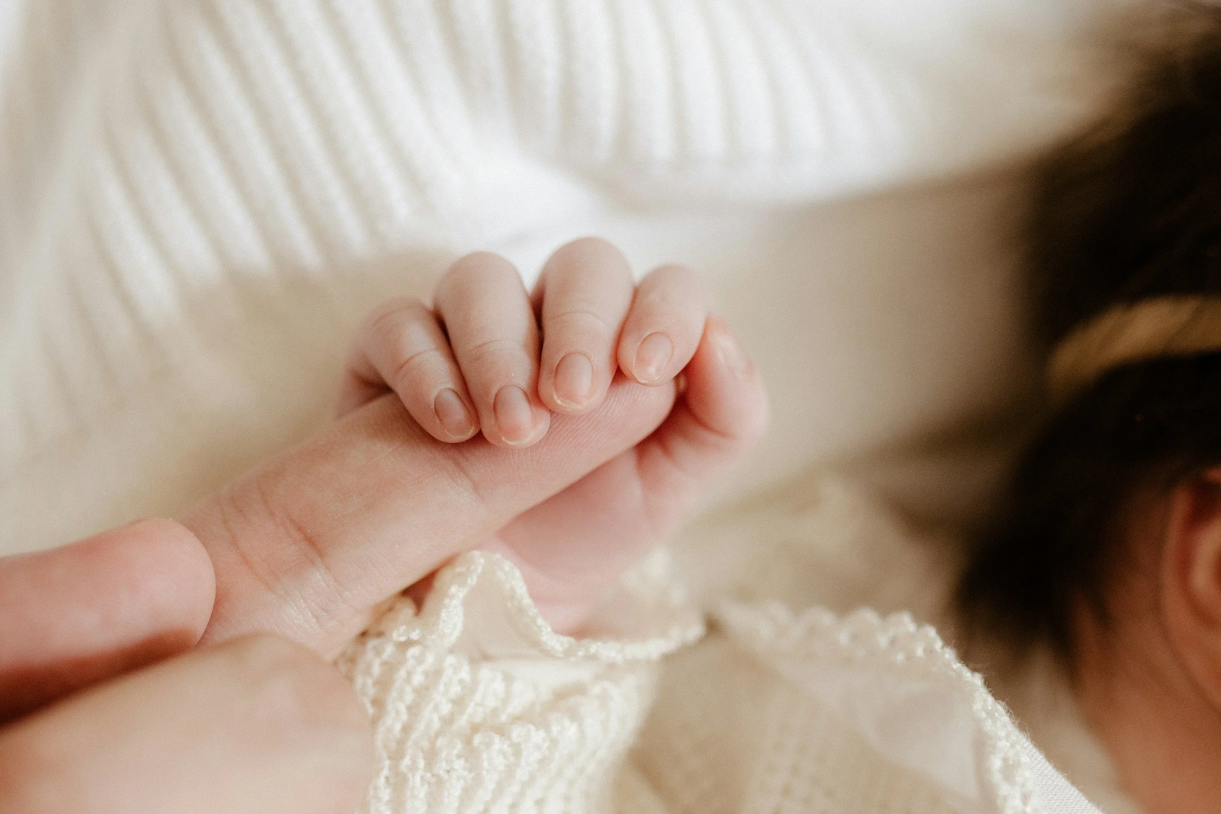 Close-up of a baby's hand gently grasping an adult's finger, with the baby wearing a white knit garment.