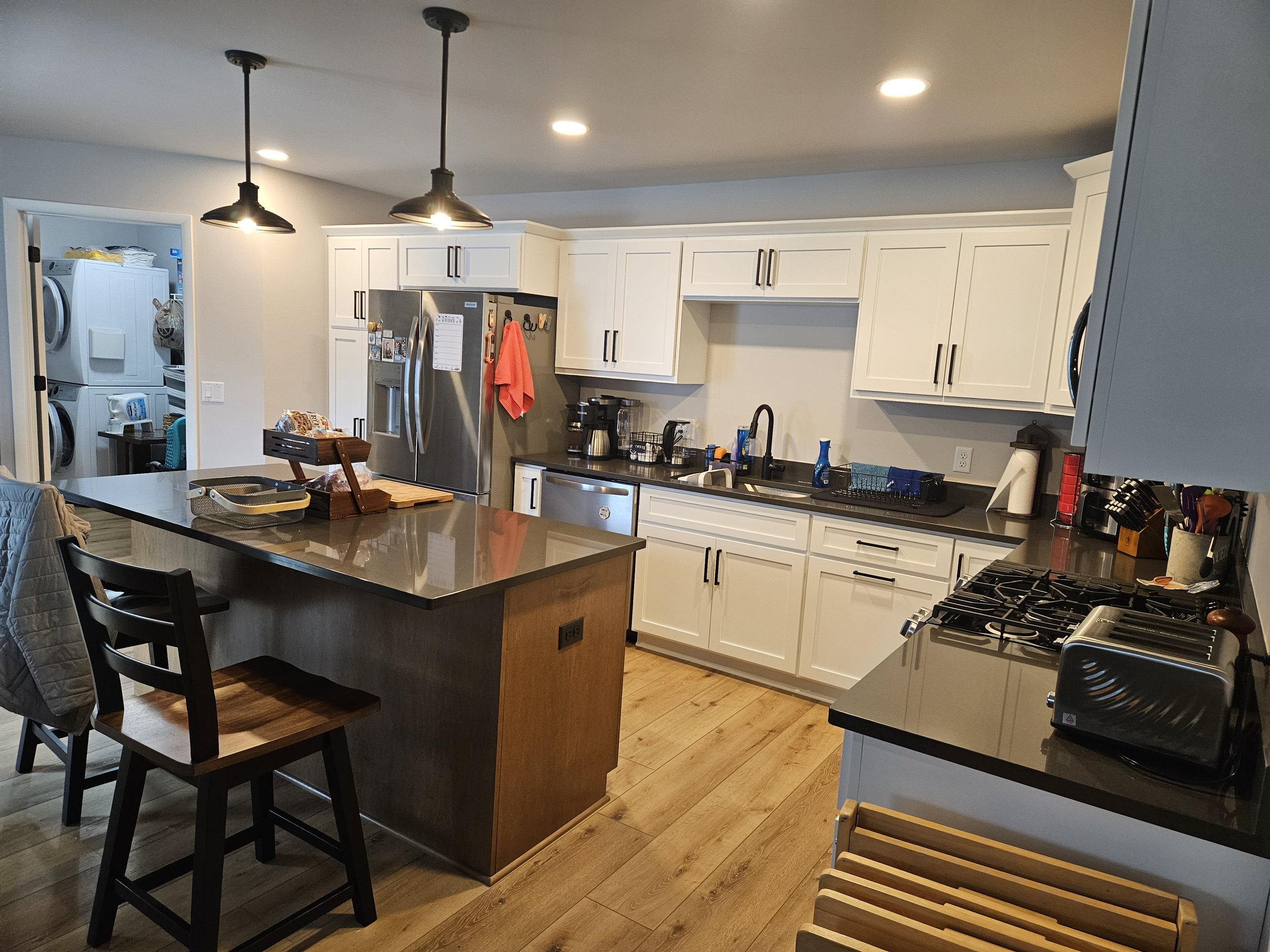 Modern kitchen with white cabinets, black countertops, stainless steel appliances, and a kitchen island with two bar stools.