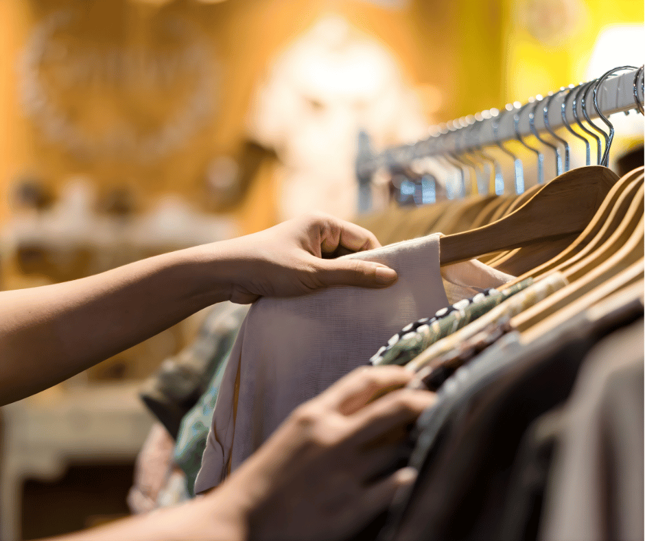 A person shopping for clothes, browsing through a rack of various garments in a store.