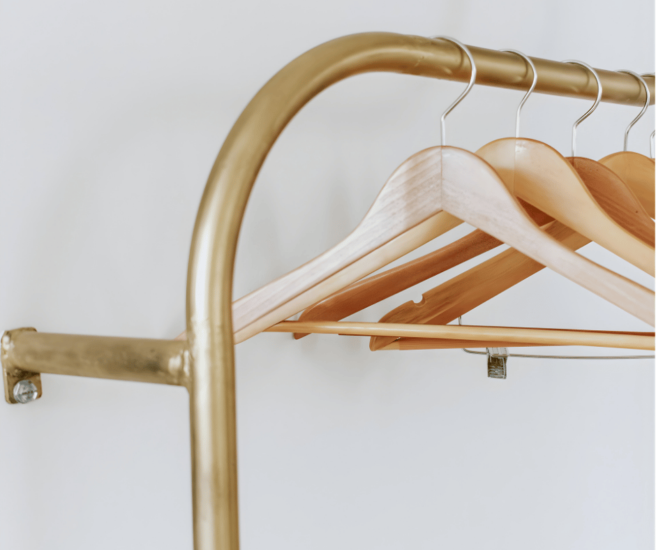 A clothing rack with wooden and beige hangers against a white wall.