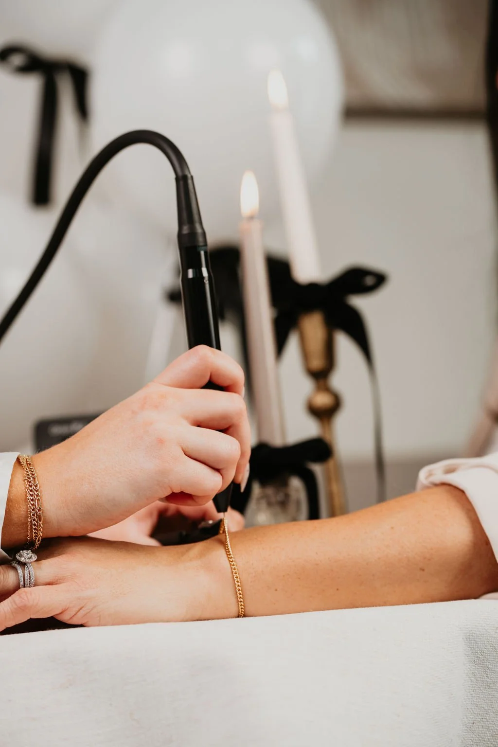 A person is getting a tattoo on their forearm using a tattoo machine, with candles and decorative items in the background.